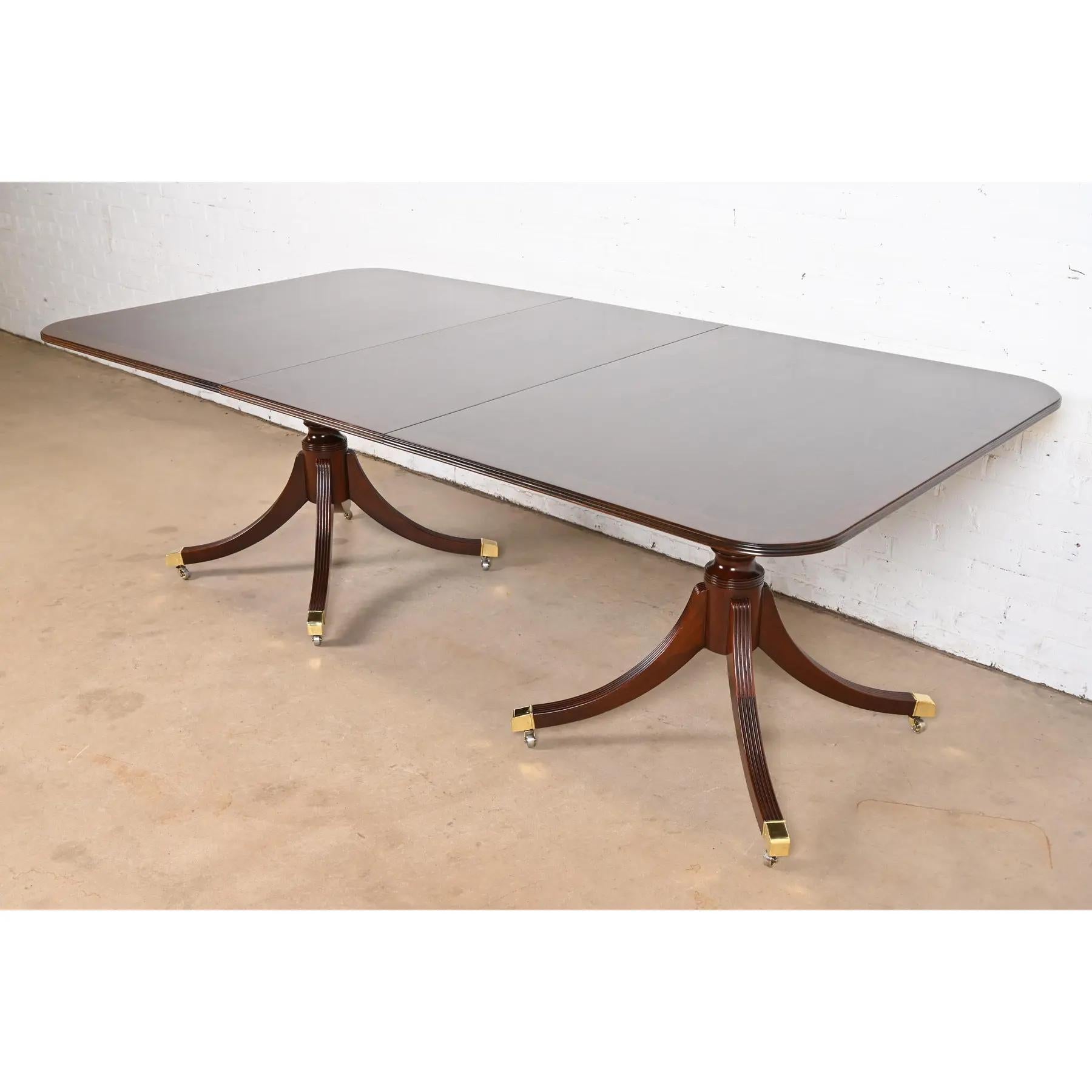 Exceptionnelle table à manger à rallonge à double piédestal de style Géorgien ou Régence.

Par Baker Furniture

USA, Circa 1980

Magnifique plateau en acajou assorti au livre, avec bandes de bois satiné, piédestaux en acajou massif sculpté, et pieds