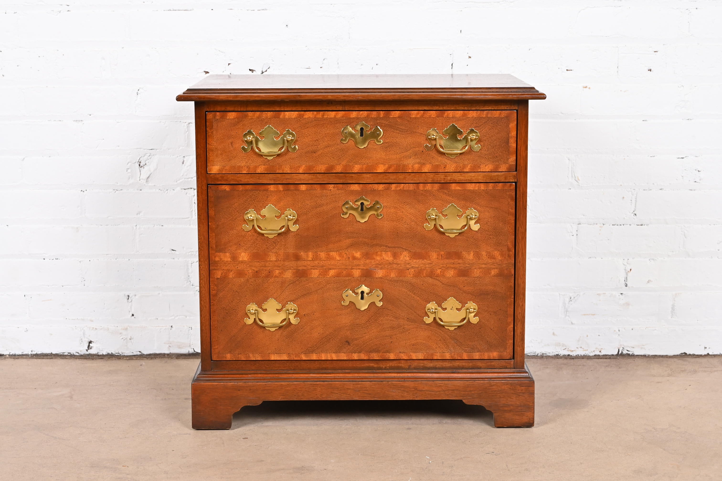 A beautiful Georgian or Chippendale style two-drawer bedside chest or commode

By Baker Furniture

USA, Circa 1980s

Mahogany, with satinwood banding and original brass hardware.

Measures: 23