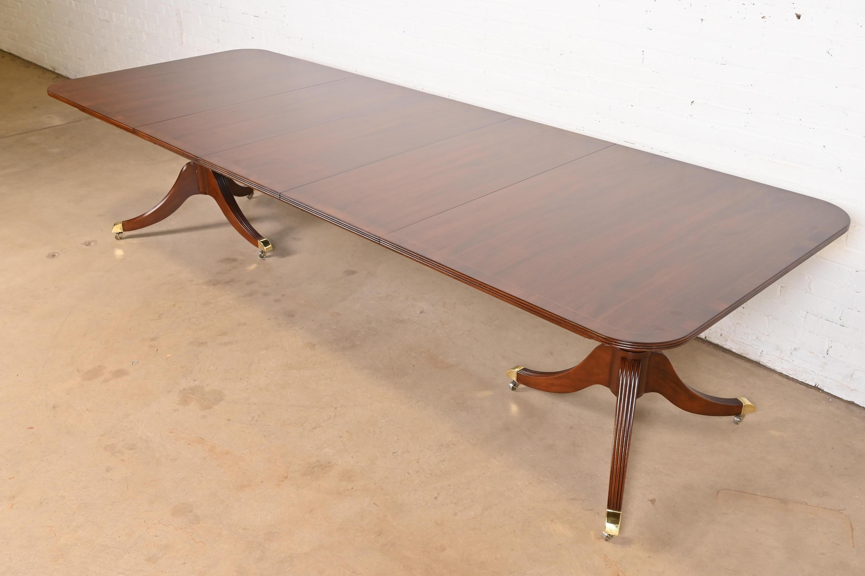 An exceptional Georgian or Regency style double pedestal extension dining table

By Baker Furniture

USA, Circa 1980s

Gorgeous banded mahogany top, with satinwood string inlay, carved solid mahogany pedestals, and brass-capped feet on