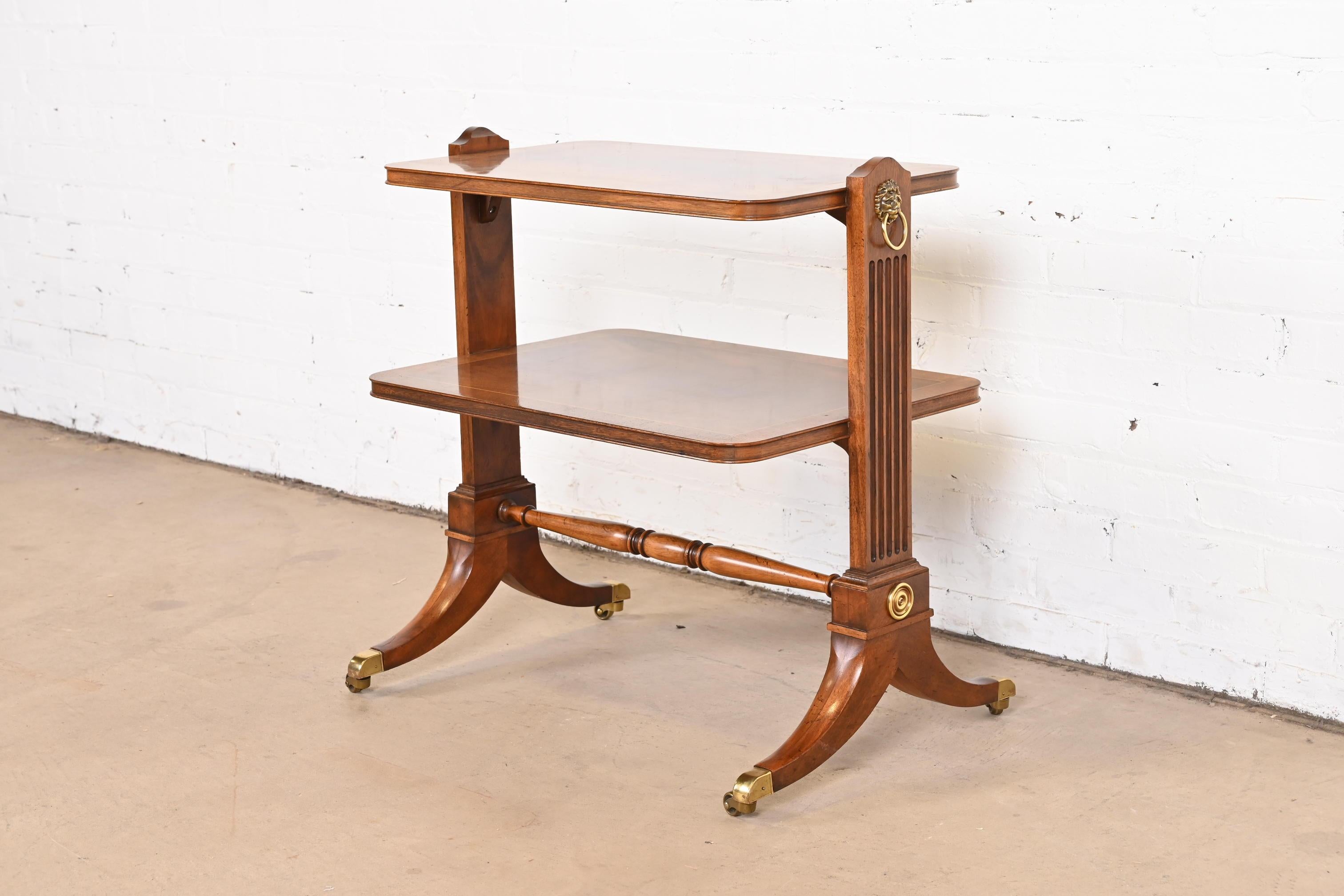 A gorgeous English Regency or Georgian style two-tier occasional side table or tea table.

By Baker Furniture.

USA, circa 1980s.

Banded flame mahogany, with satinwood string inlay, and original brass hardware and accents.

Measures: 27.5