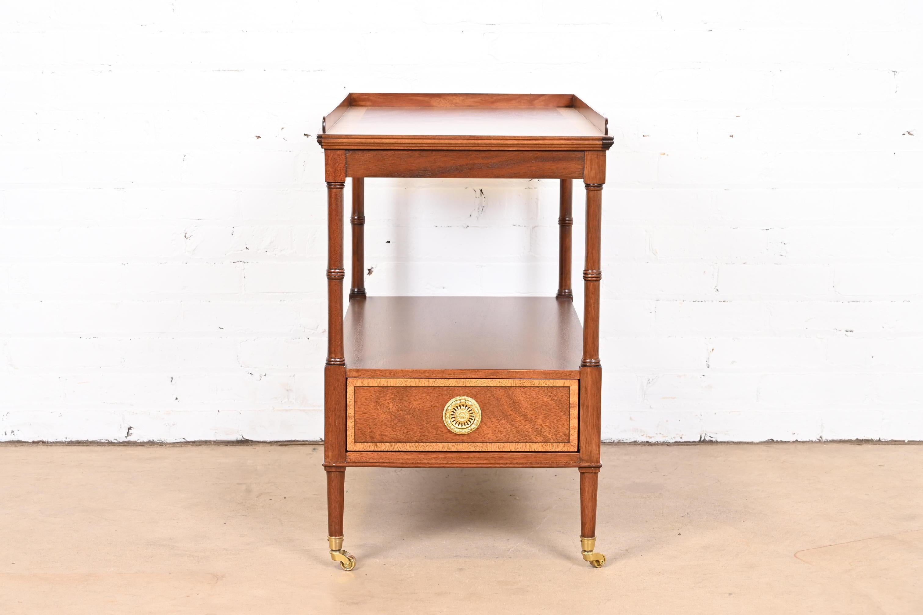 A gorgeous Georgian or Regency style two-tier nightstand, tea table, or occasional side table

By Baker Furniture

USA, Circa 1980s

Mahogany, with satinwood banding and original brass hardware and casters.

Measures: 16