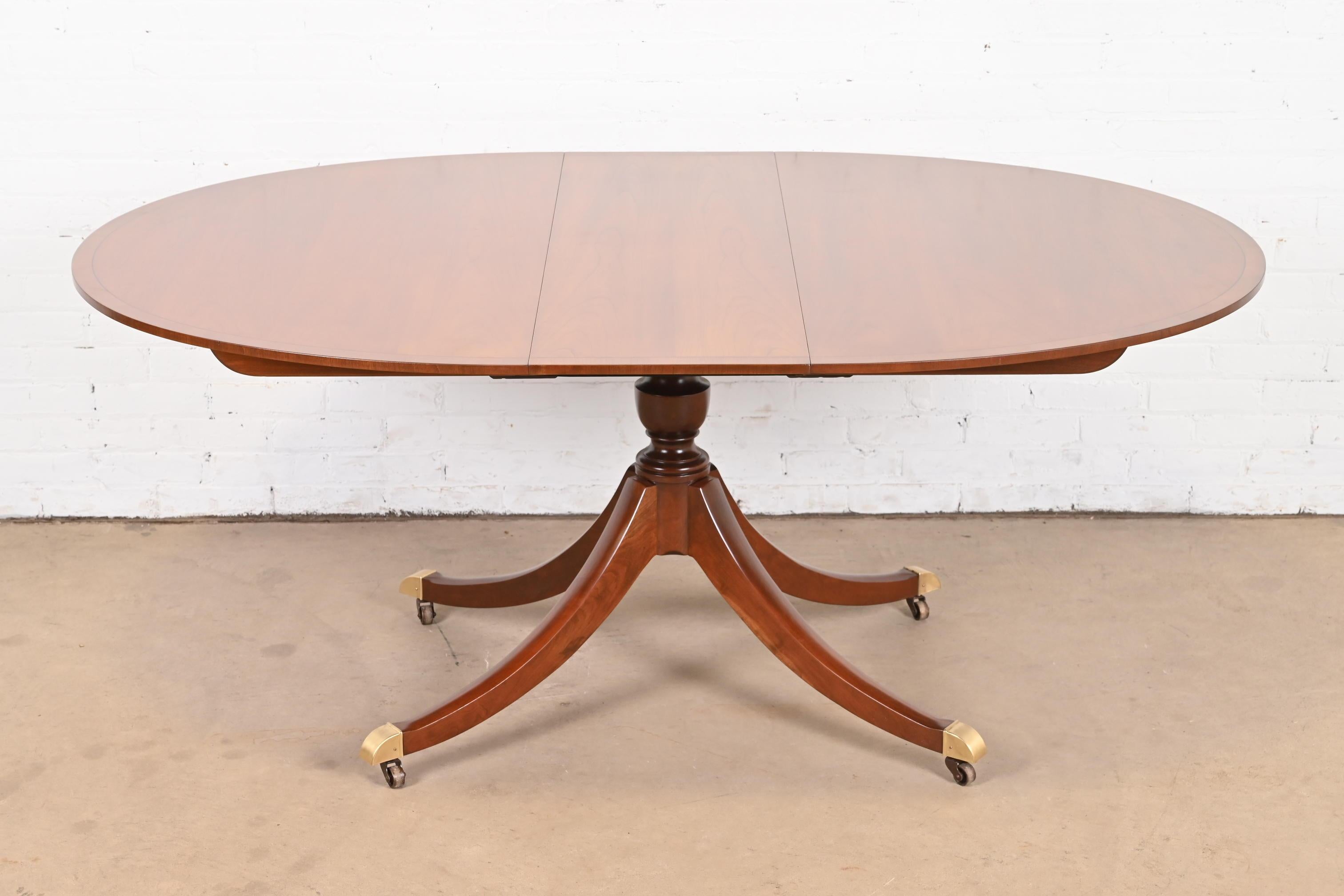 An exceptional Georgian or Regency style single pedestal extension dining table

By Baker Furniture

USA, Circa 1980s

Beautiful book-matched cherry wood, with ebony string inlay, carved solid cherry wood pedestal, and brass-capped feet on
