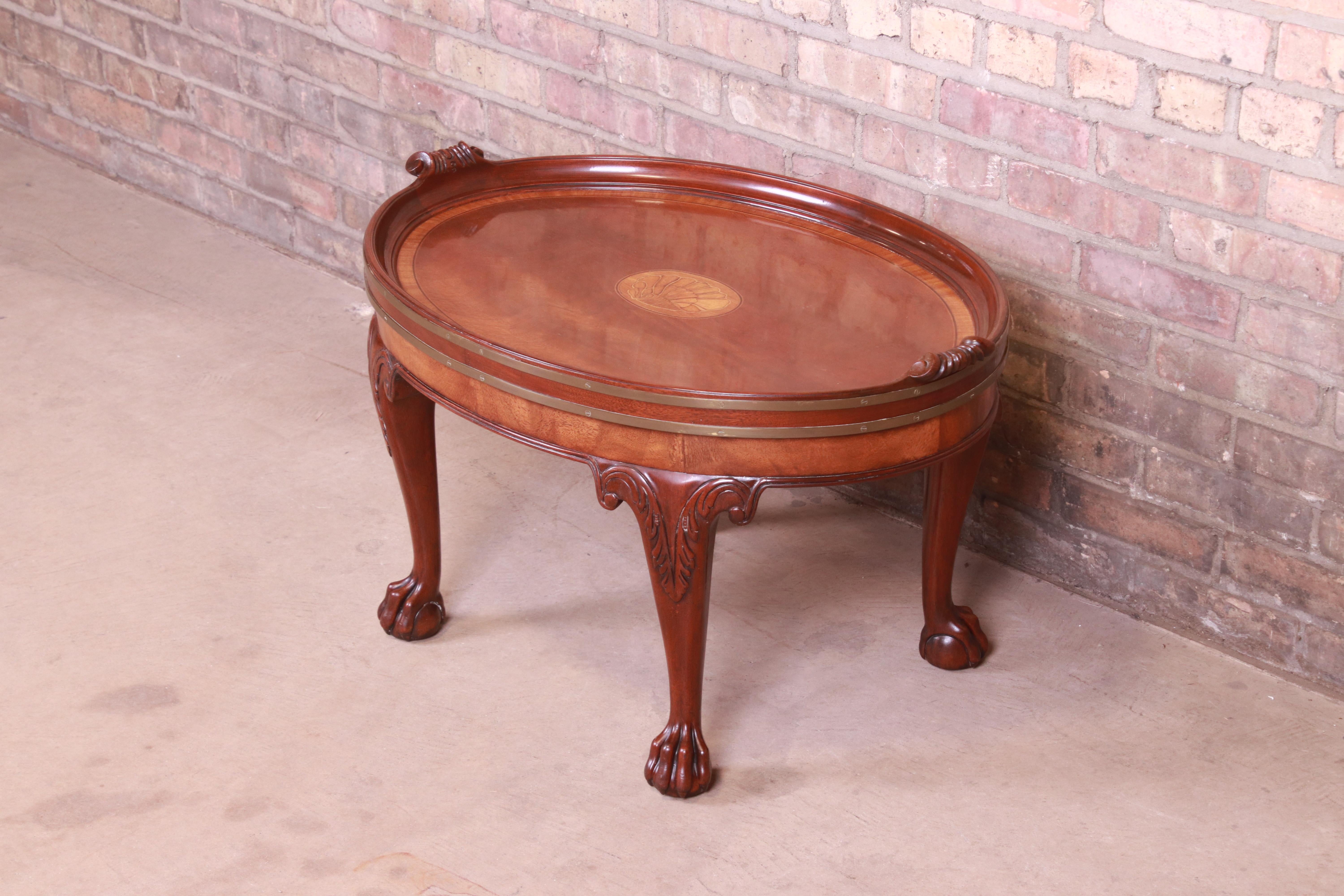 A gorgeous George III or Chippendale style coffee or cocktail table

By Baker Furniture

USA, Circa 1980s

Carved mahogany, with inlaid shell marquetry, ball and claw feet, and brass trim.

Measures: 31.25