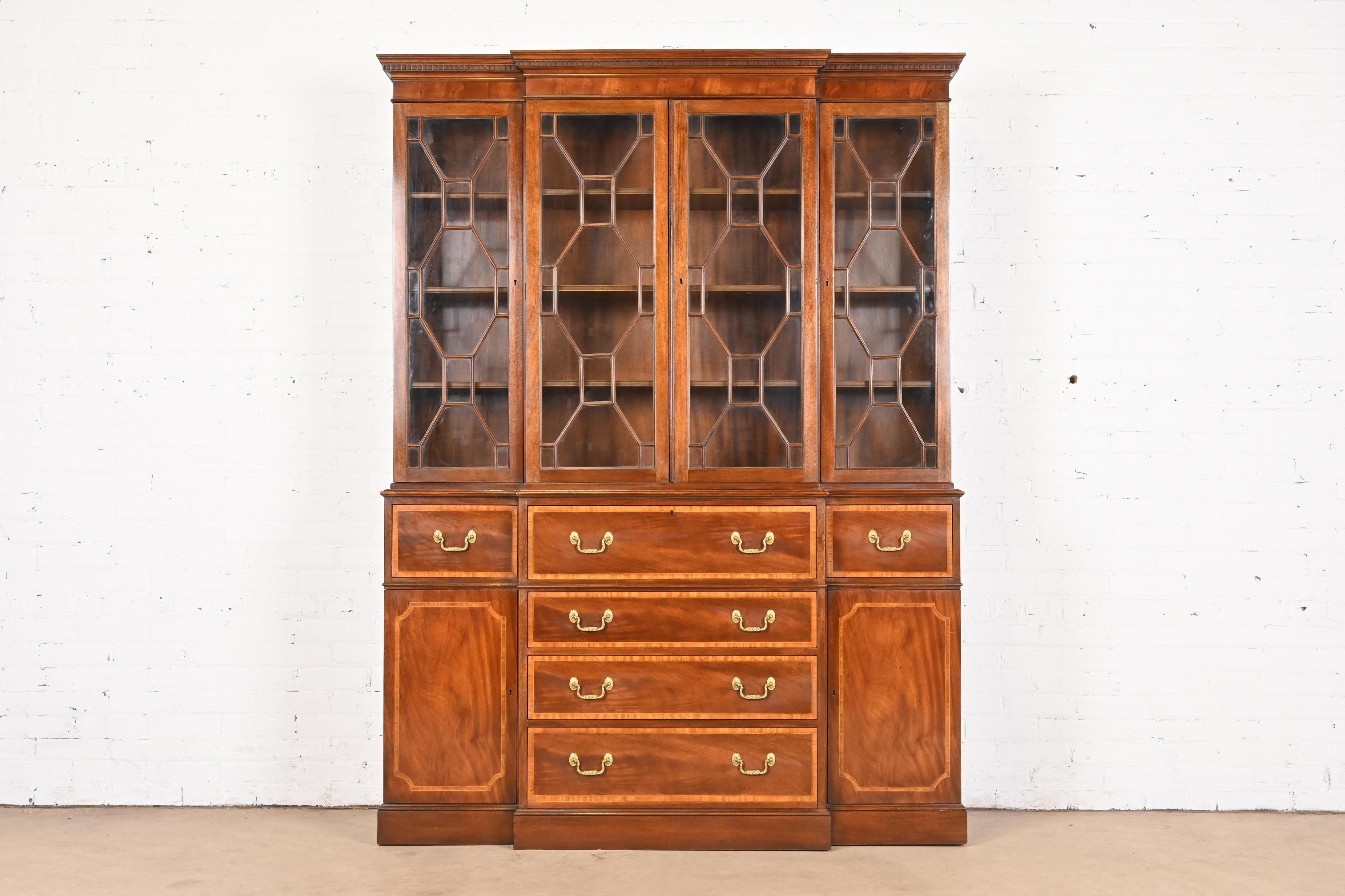 A gorgeous Georgian or Chippendale style breakfront bookcase or dining cabinet with drop front secretary desk

By Baker Furniture

USA, Circa 1980s

Carved mahogany, with inlaid satinwood banding, mullioned glass front doors, and original brass
