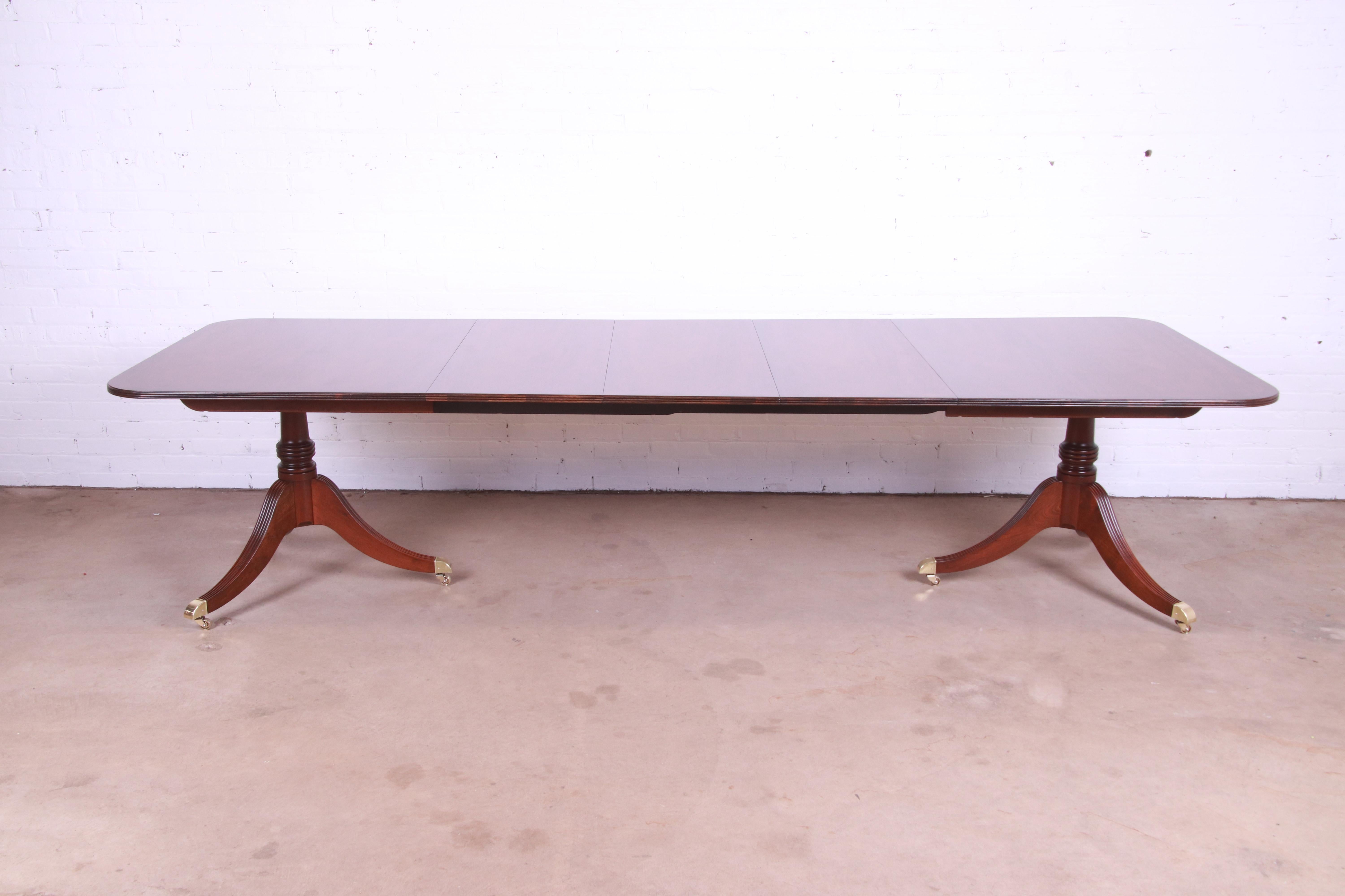 An exceptional Georgian style double pedestal extension dining table.

By Baker Furniture

USA, mid-20th century.

Book-matched mahogany, with satinwood string inlay, carved solid mahogany pedestals, brass-capped feet, and brass