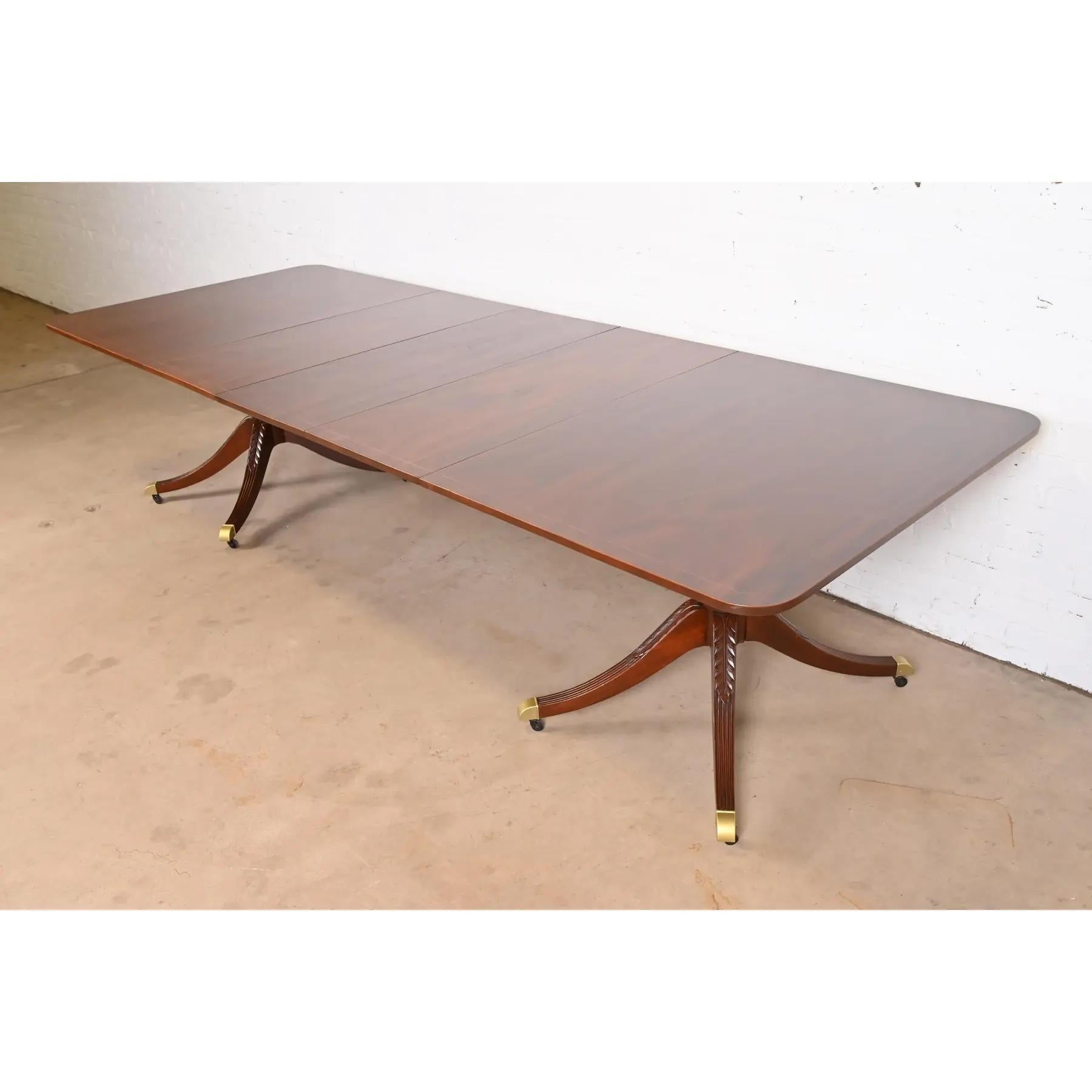 An exceptional Georgian or Regency style double pedestal extension dining table

By Baker Furniture

USA, Mid-20th Century

Gorgeous book-matched mahogany, with satinwood string inlaid banding, carved solid mahogany pedestals, and brass capped feet
