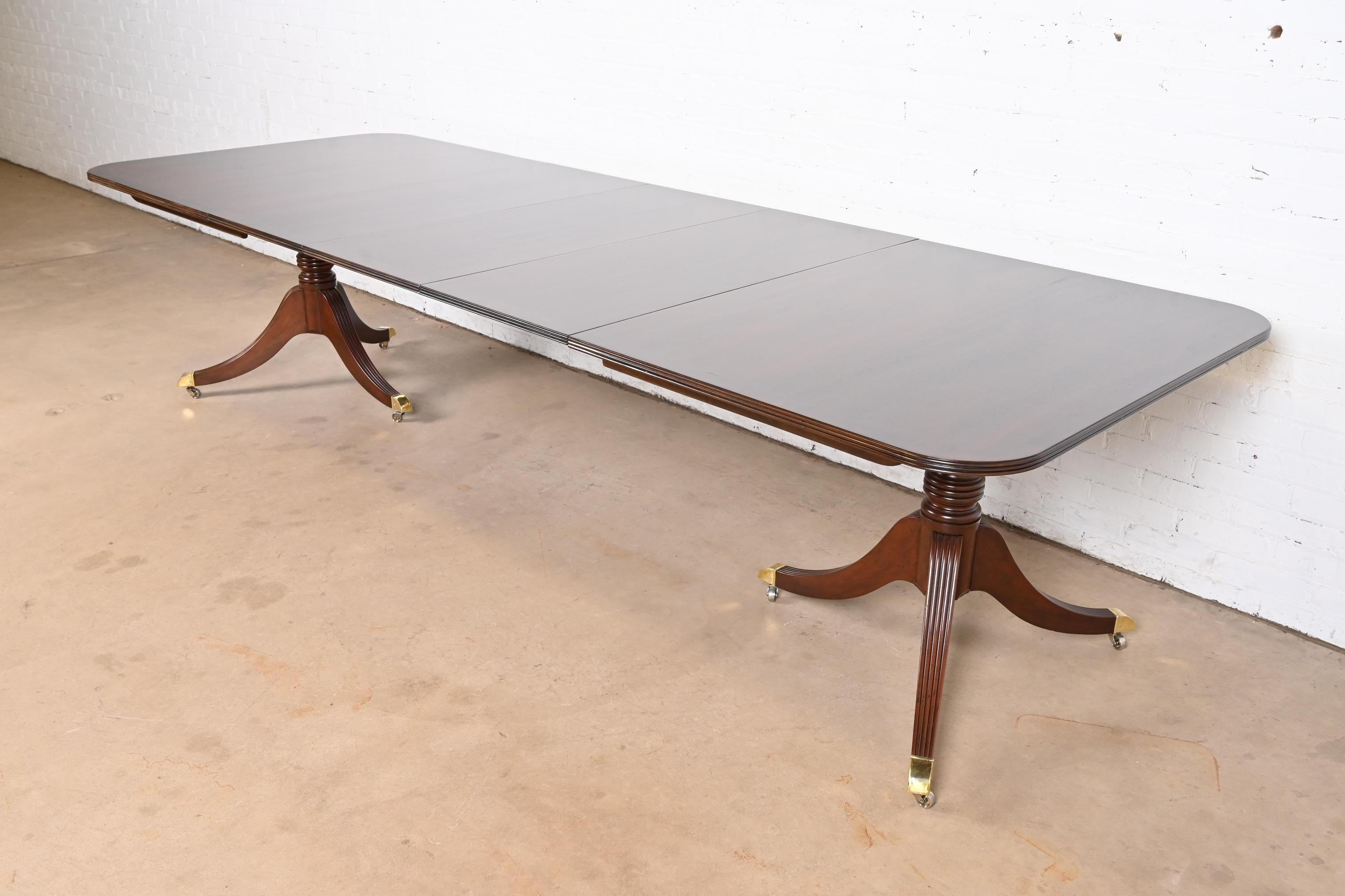Exceptionnelle table à manger à rallonge à double piédestal de style Géorgien ou Régence.

Par Baker Furniture

USA, Circa 1980

Magnifique plateau en acajou bagué, avec des piédestaux en acajou massif sculpté, et des pieds coiffés de laiton sur des