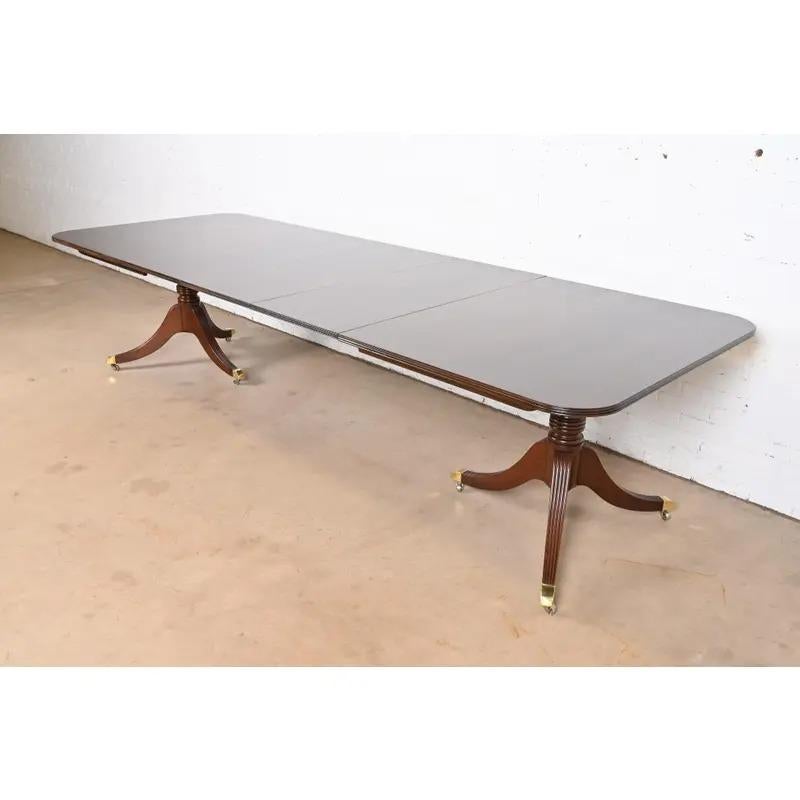 Exceptionnelle table à manger à rallonge à double piédestal de style Géorgien ou Régence.

Par Baker Furniture

USA, Circa 1980

Magnifique plateau en acajou bagué, avec des piédestaux en acajou massif sculpté, et des pieds coiffés de laiton sur des