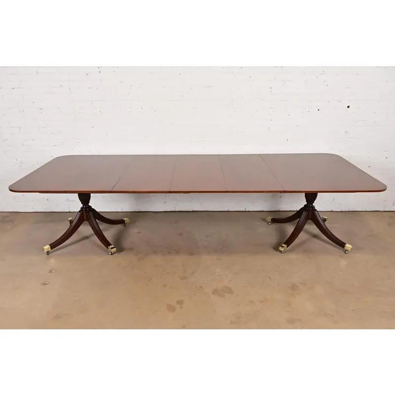 An exceptional Georgian or Regency style double pedestal extension dining table

By Baker Furniture

USA, Circa 1980s

Gorgeous book-matched mahogany top, with rosewood banding, carved solid mahogany pedestals, and brass-capped feet on brass