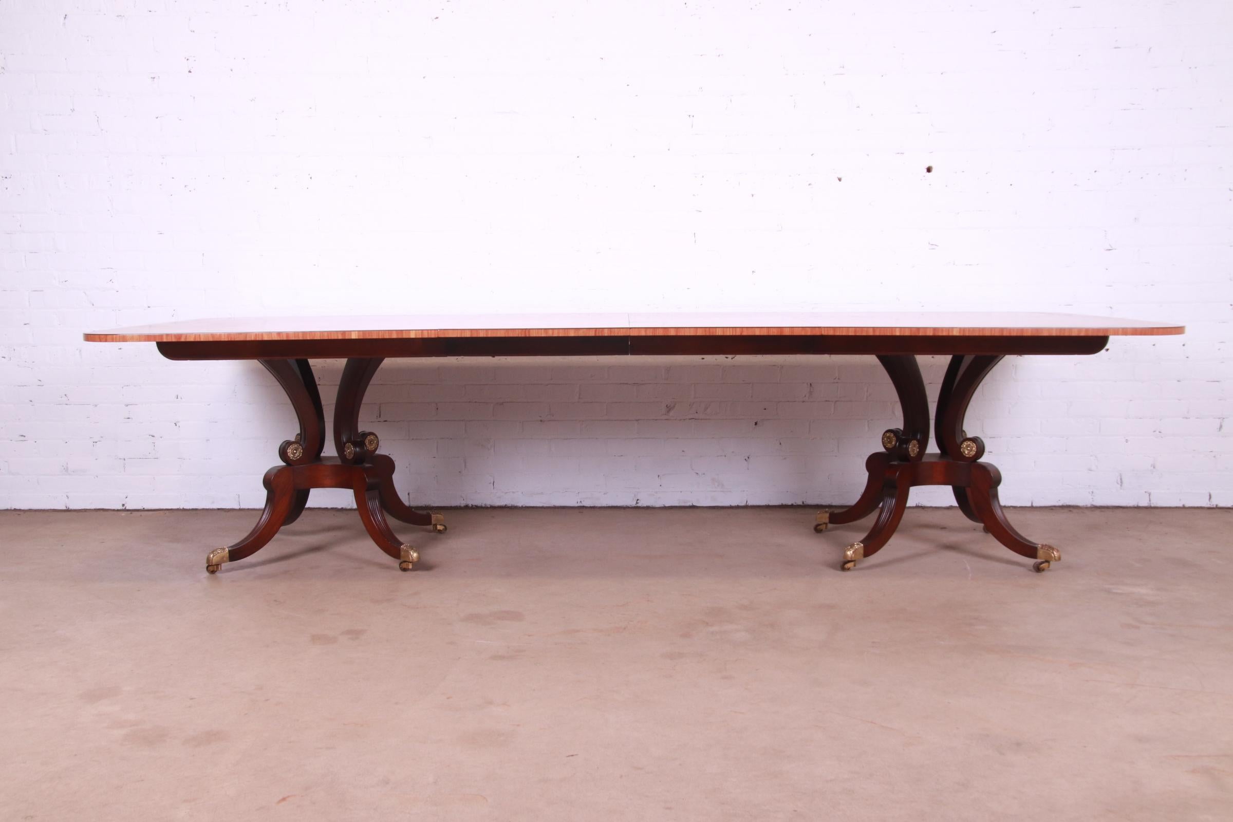 An exceptional Georgian or Regency style double pedestal extension dining table

By Baker Furniture

USA, late 20th century

Gorgeous banded satinwood top, with carved solid mahogany pedestals, brass accents, brass-capped feet, and brass