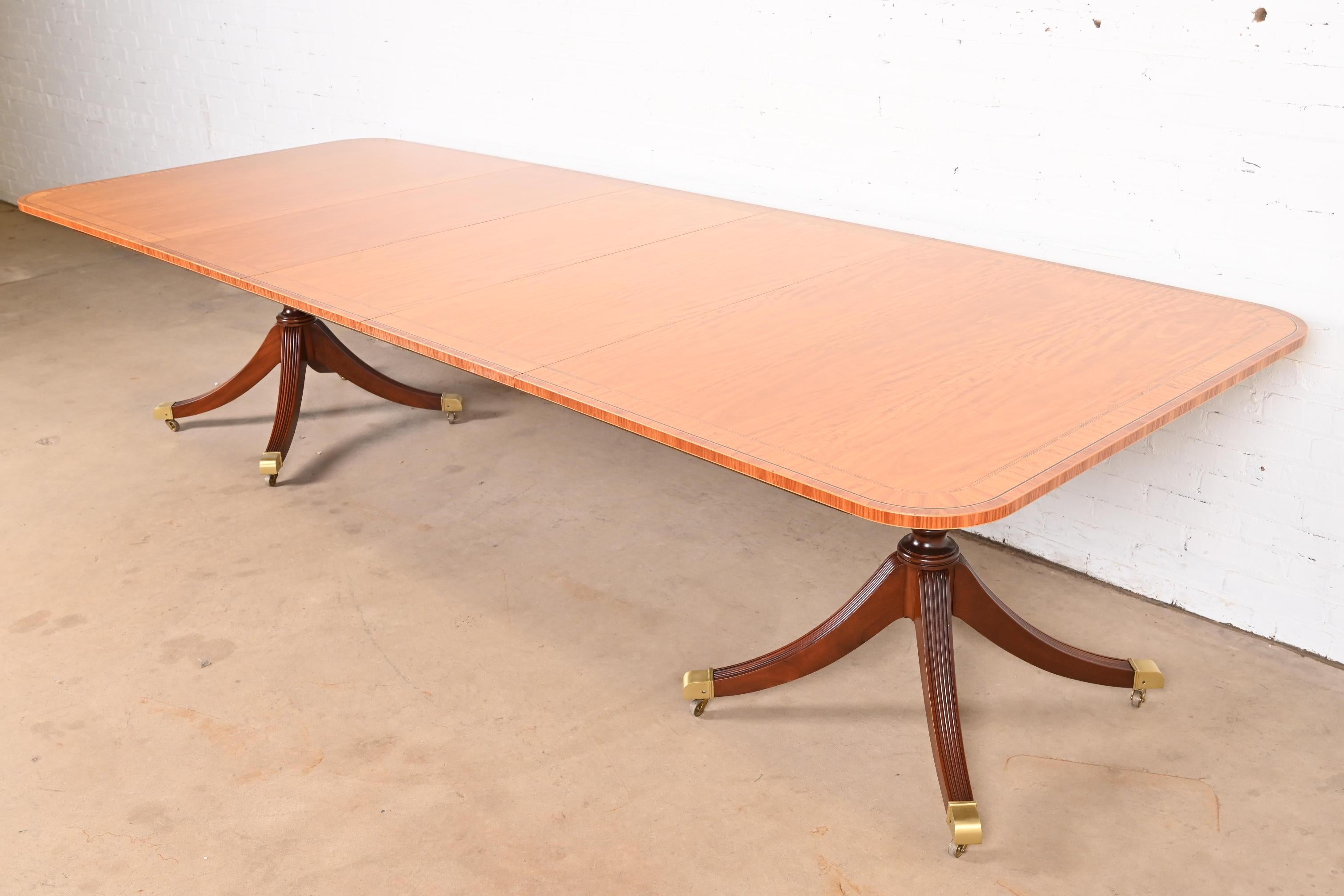 Exceptionnelle table à manger à rallonge à double piédestal de style Géorgien ou Régence.

Par Baker Furniture

USA, Circa 1980

Magnifique plateau en bois de satin à bandes assorties, avec des piédestaux en acajou massif, et des pieds coiffés de