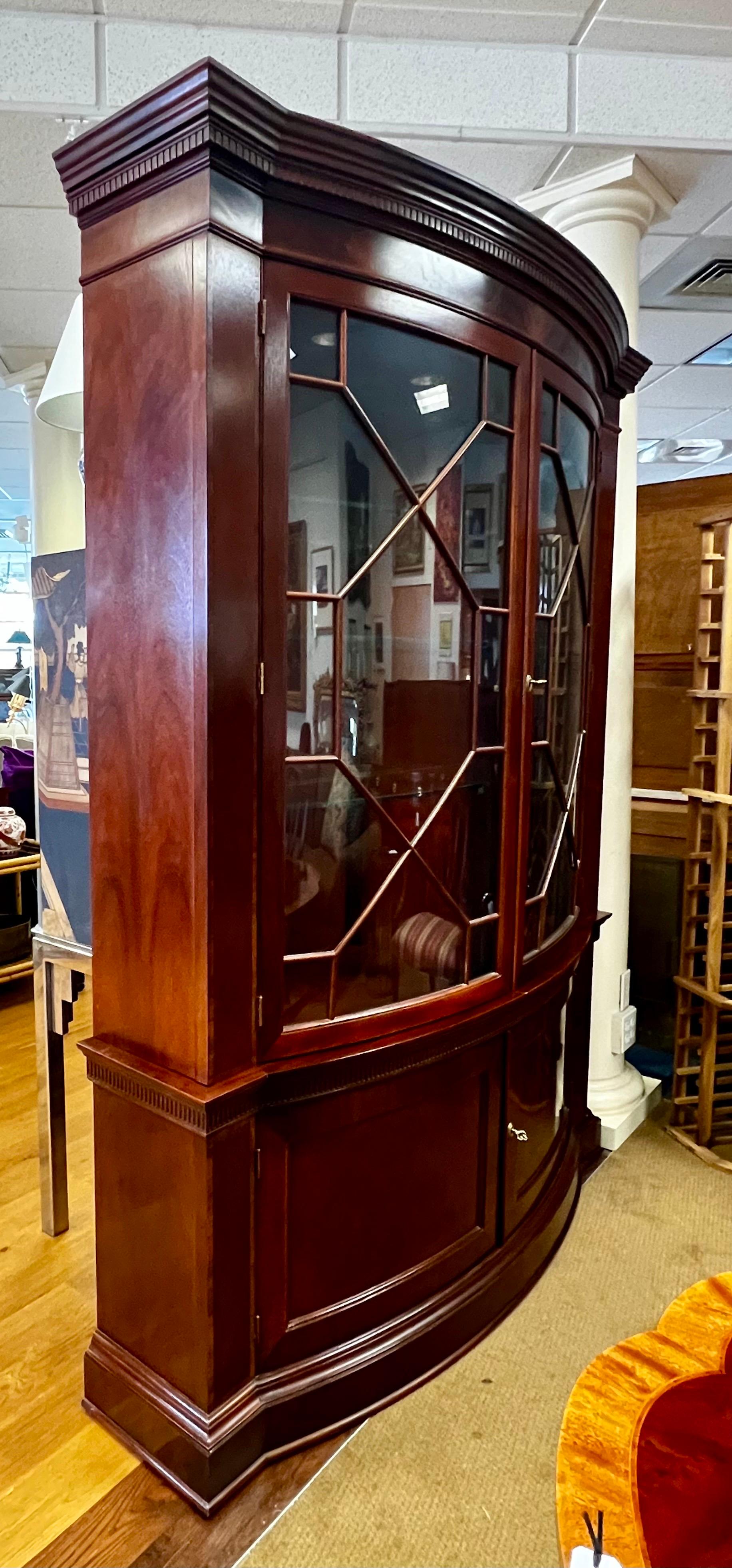 Sought after Baker Furniture Historic Charleston mahogany china cabinet/breakfront. Features two-piece bow-front design, upper case with a cornice top over dentil molding and glazed glass doors with escutcheon and fretwork. Also has lighted interior