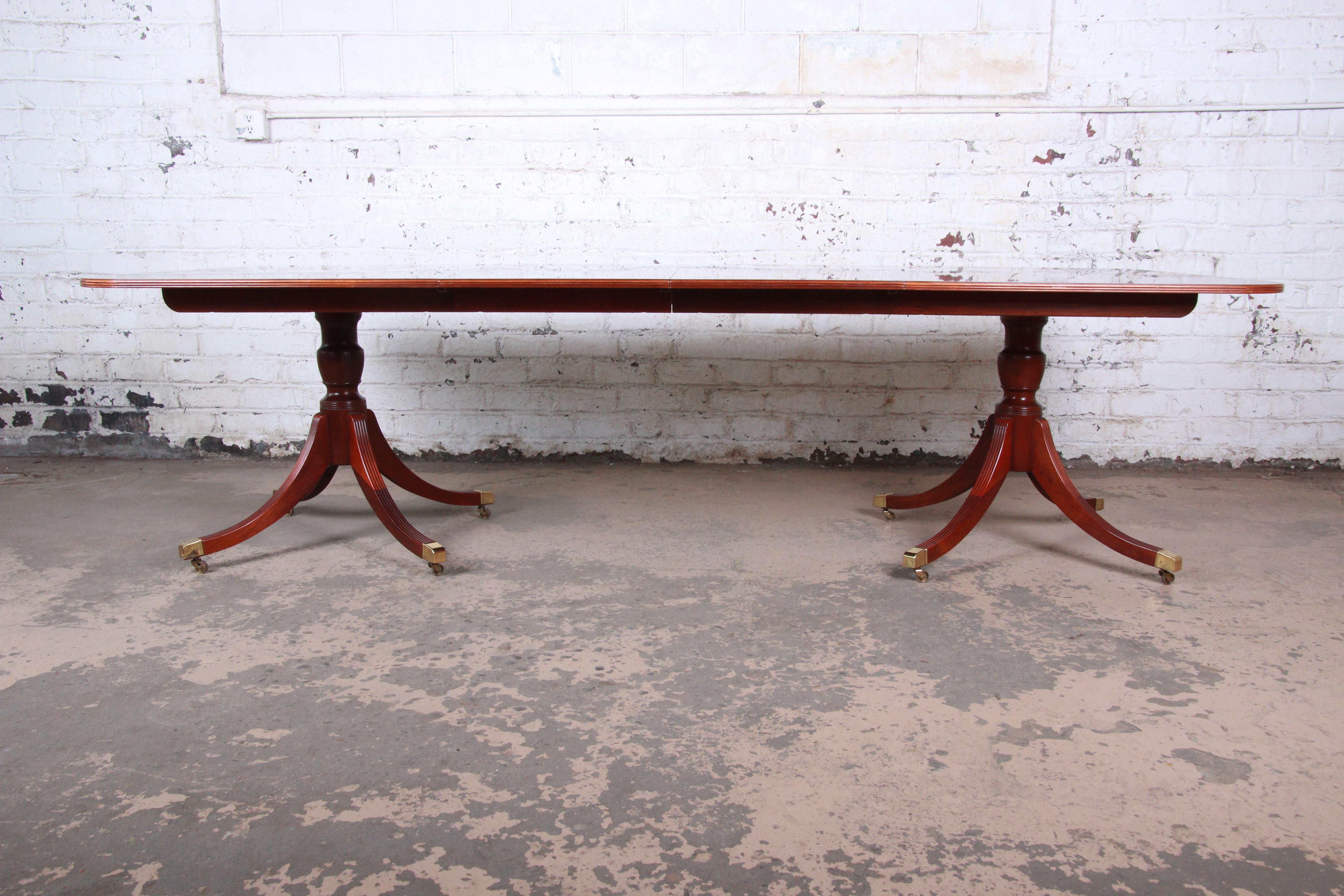 An exceptional Georgian banded and inlaid mahogany dining table from the Historic Charleston Collection by Baker Furniture. The double pedestal table features gorgeous mahogany wood grain with inlaid satinwood and a nice traditional English style.