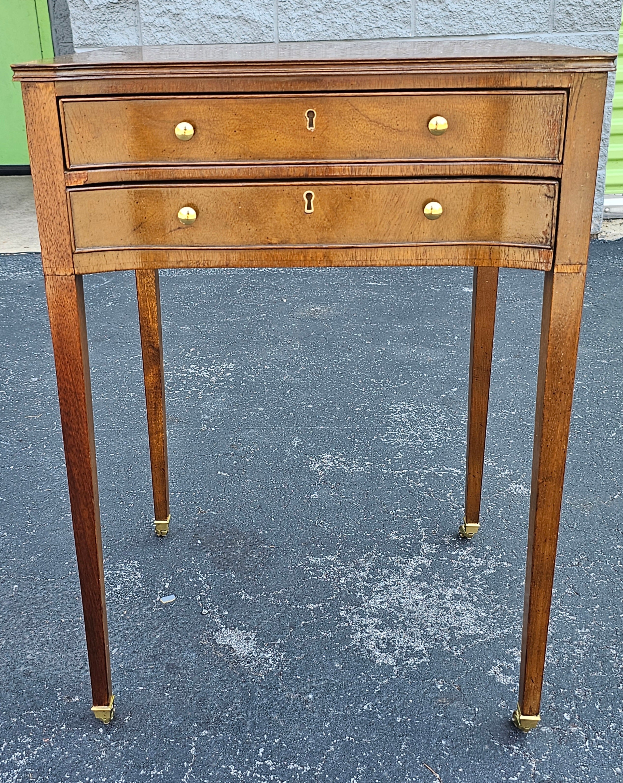 A Baker Furniture Company Hictoric Charleston Collection Two Drawer Side Table with tapered legs termination with brass savots on Wheels. Measures 19.25