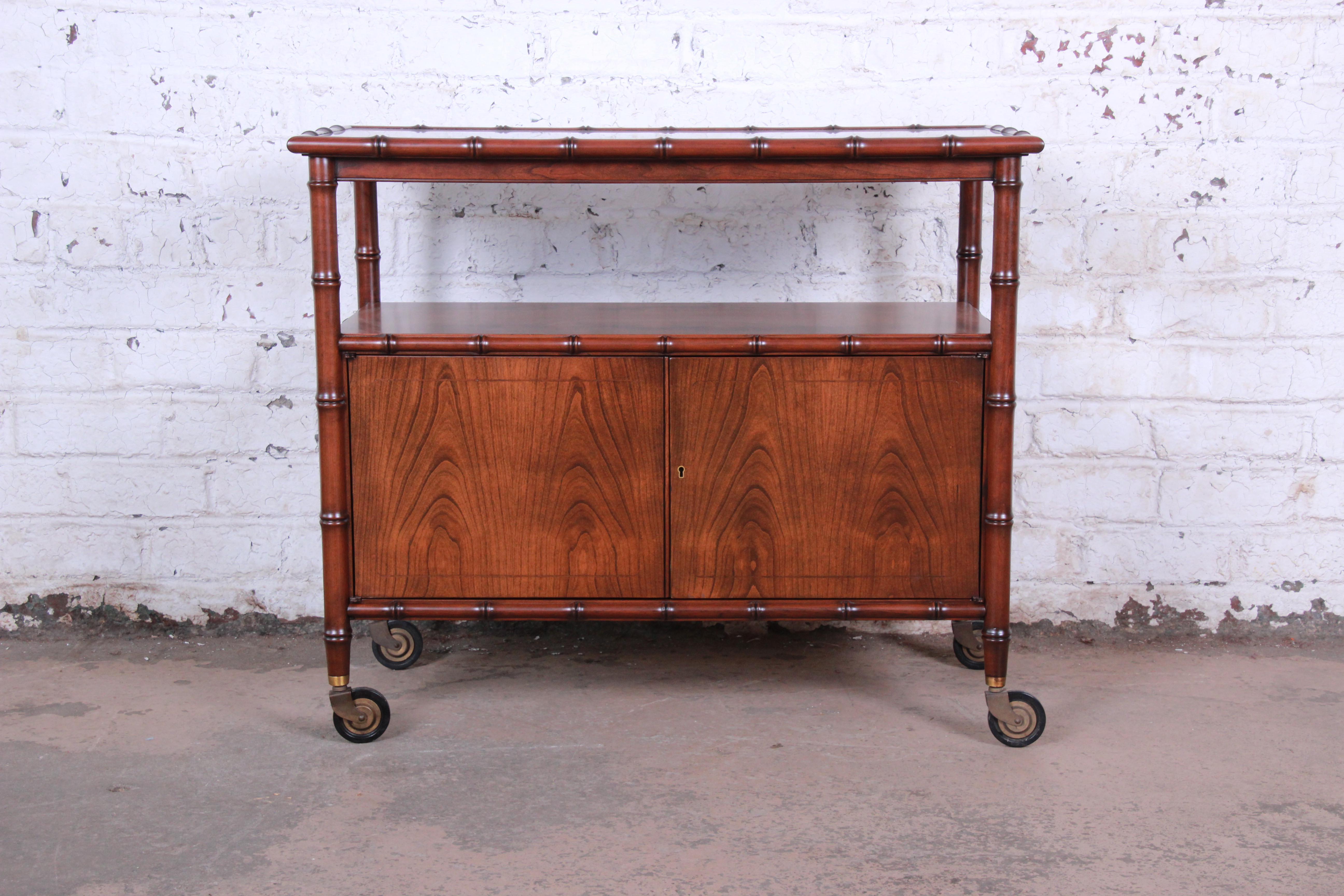 A gorgeous Mid-Century Modern Hollywood Regency bar cart by Baker Furniture. The cart features stunning book-matched walnut wood grain, with a unique faux bamboo frame. It offers good storage and serving space, with a black laminate top that extends
