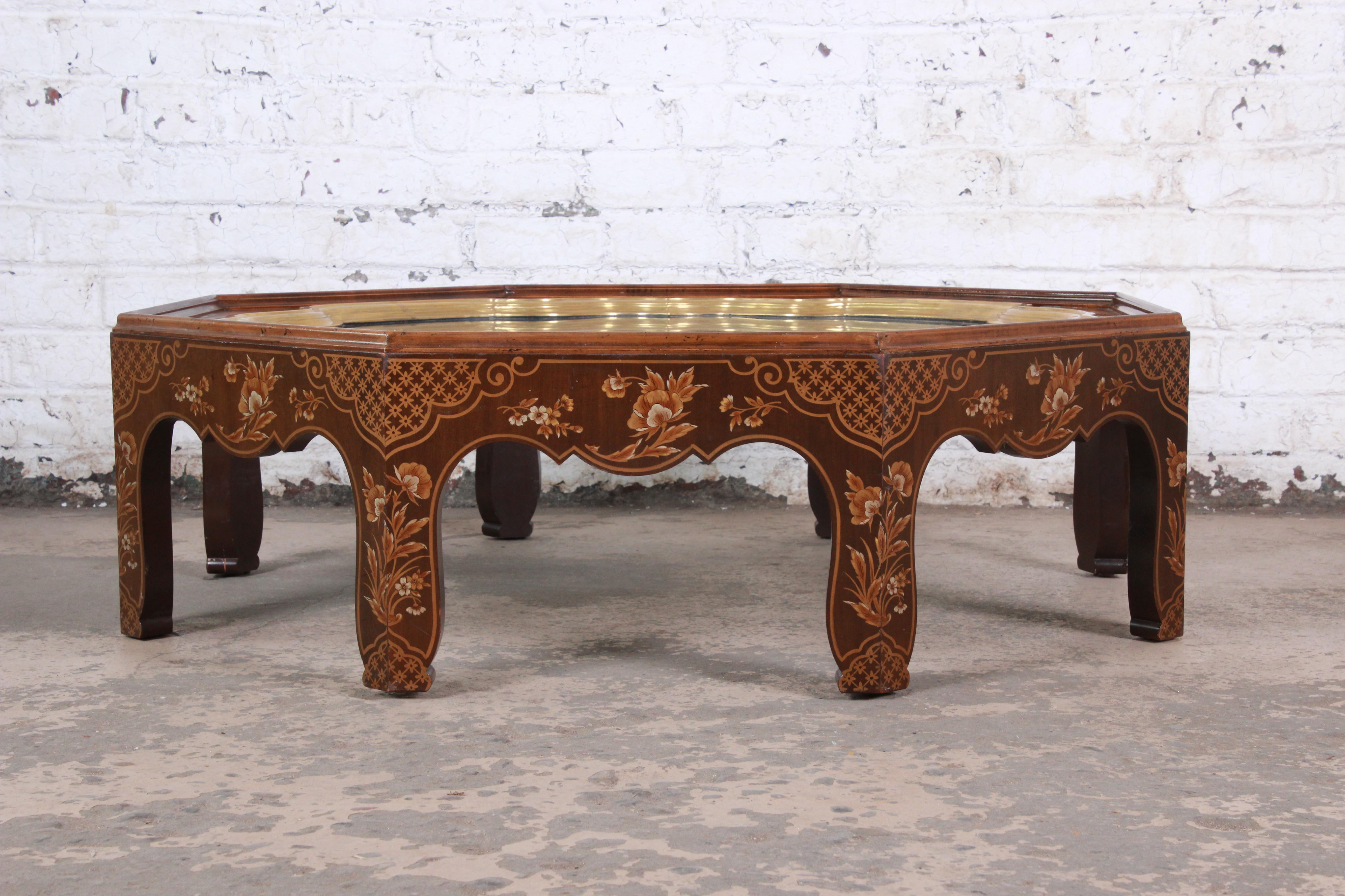 A gorgeous Hollywood Regency chinoiserie octagonal coffee or cocktail table by Baker Furniture. The table features beautiful hand painted floral Asian designs along the sides and a stunning brass framed inset glass top. The original Baker label is