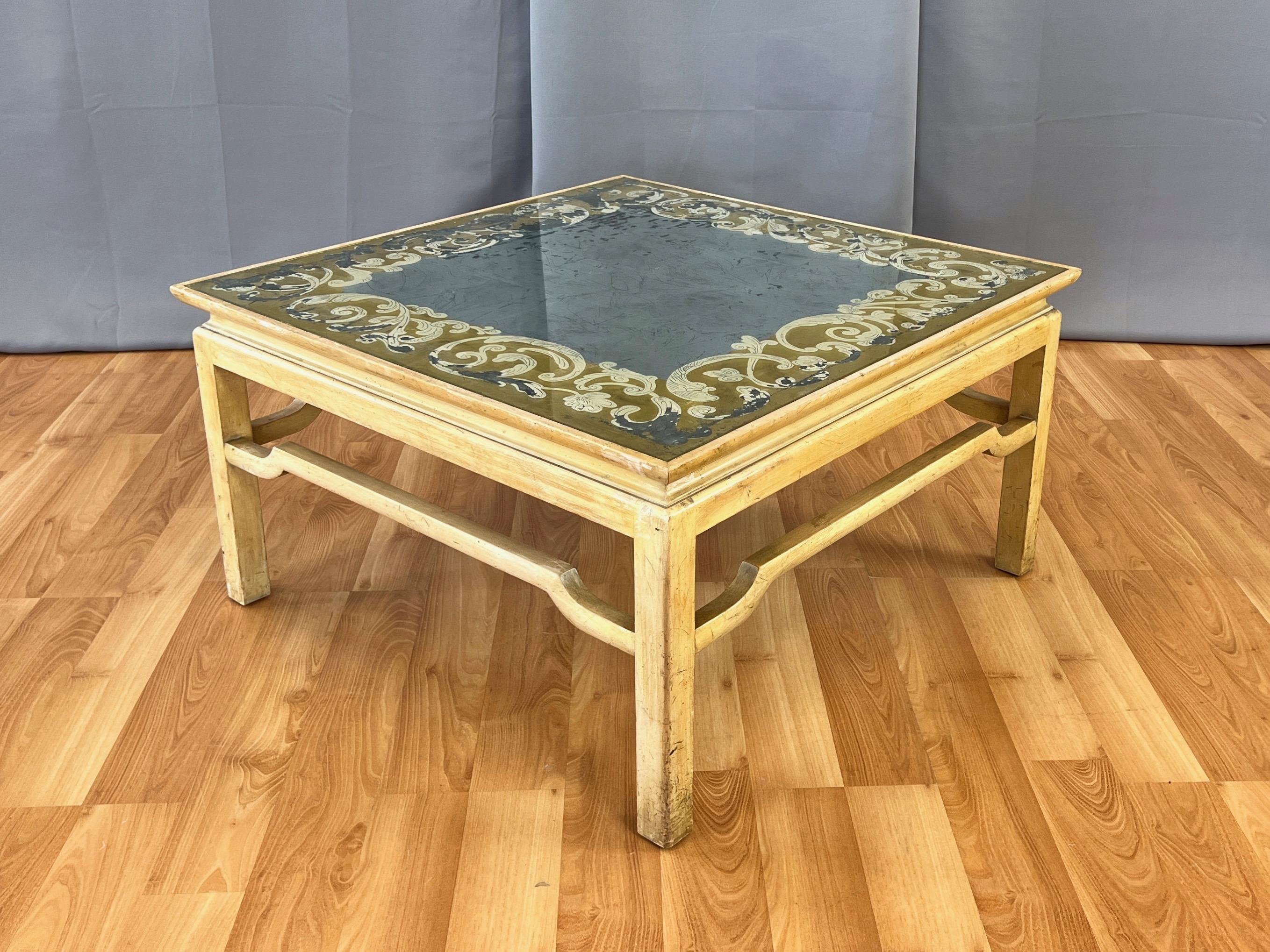 A very striking and uncommon circa 1950 Hollywood Regency square coffee table with gold and silver leaf verre églomisé top by Baker Furniture Company.

Inset glass top is reverse painted with a lovely Italianate foliate-motif scroll border in fine