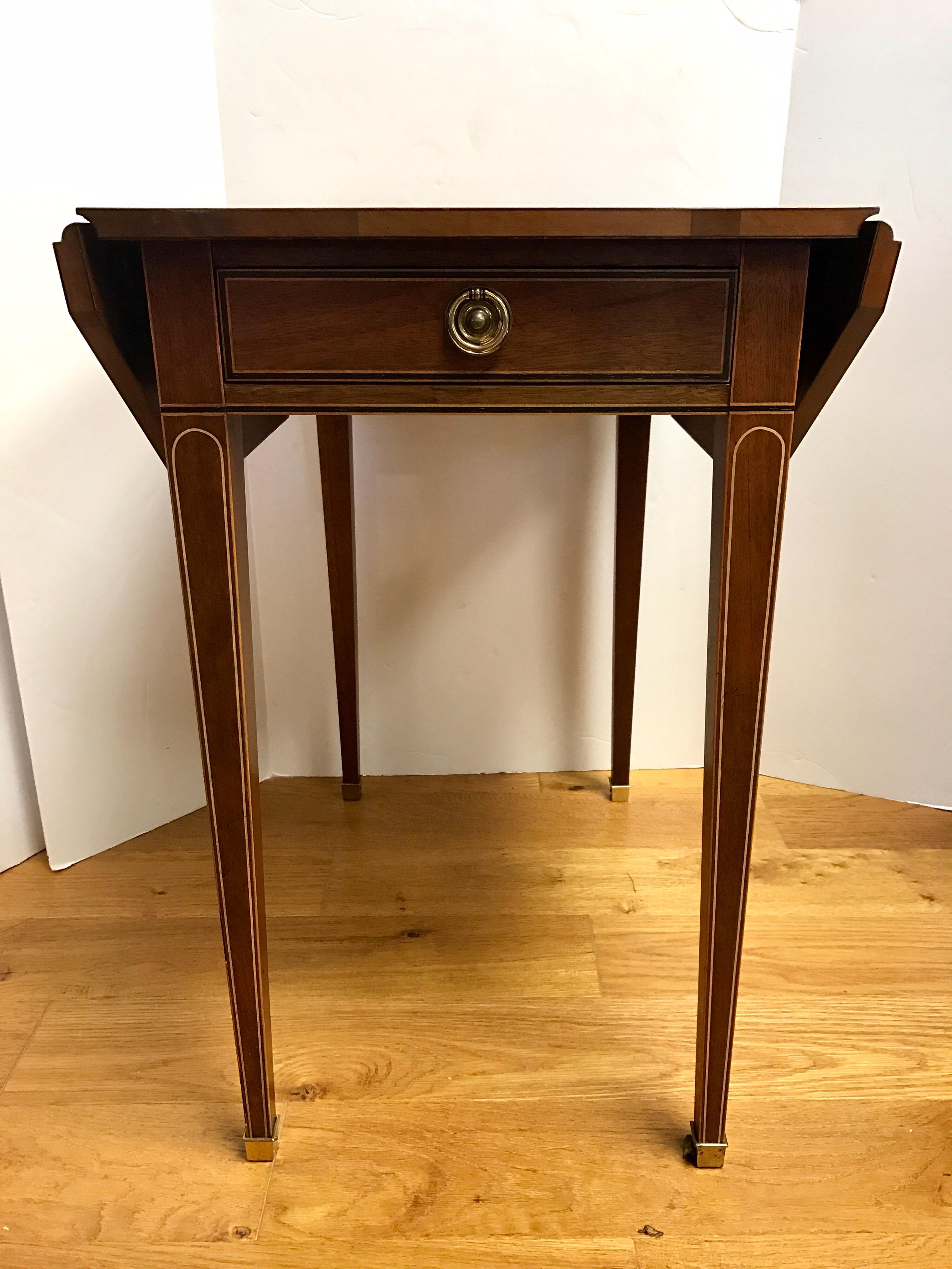 Baker Furniture mahogany drop leaf table that goes from seventeen inches wide to 31 inches when both leaves are up. Features brass feet, an elegant inlay and a lone center drawer.