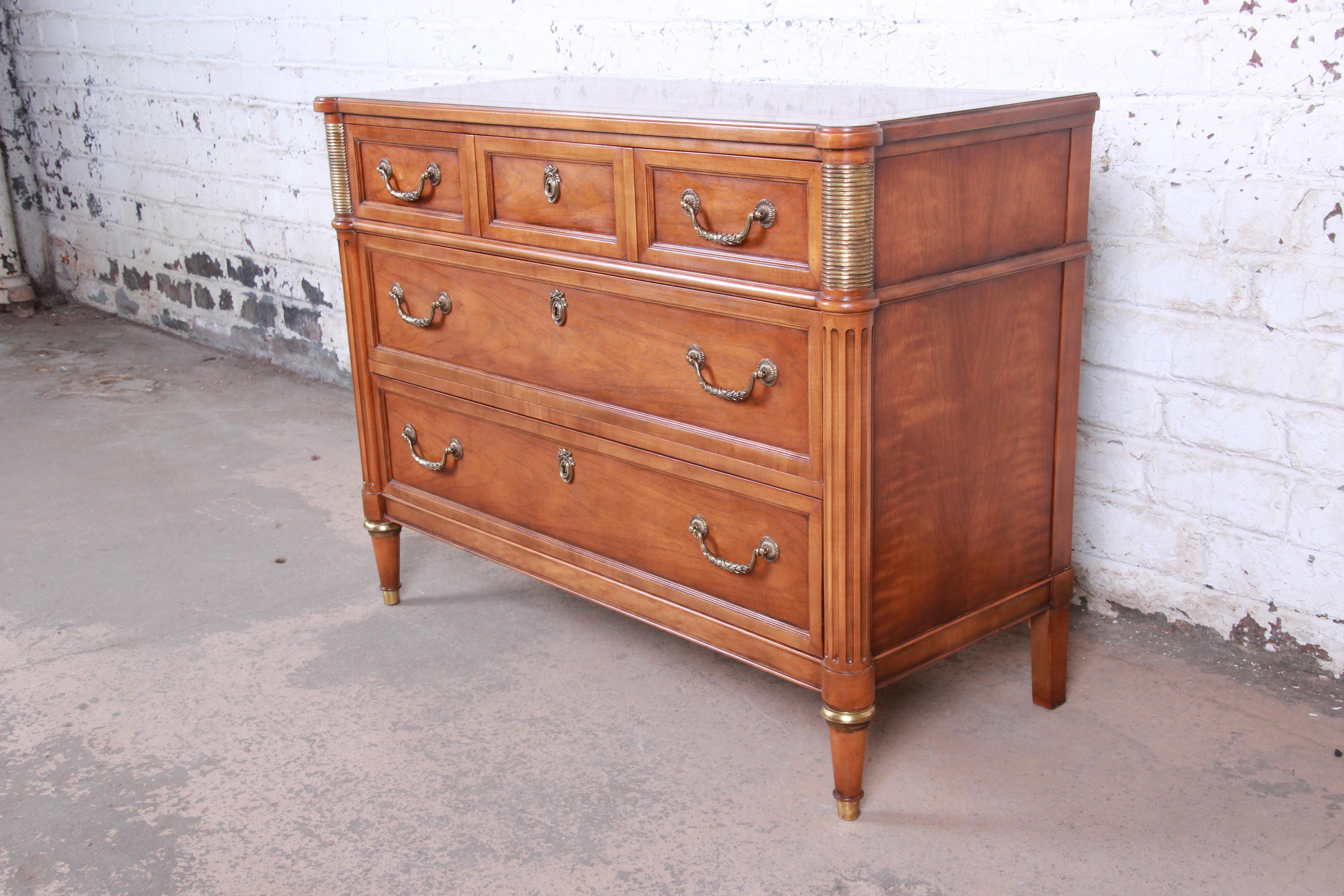A gorgeous Louis XVI style French Regency three-drawer bachelor chest of drawers by Baker Furniture. The dresser features beautiful walnut wood grain and nice brass details. It offers good storage, with three deep dovetailed drawers. All hardware is