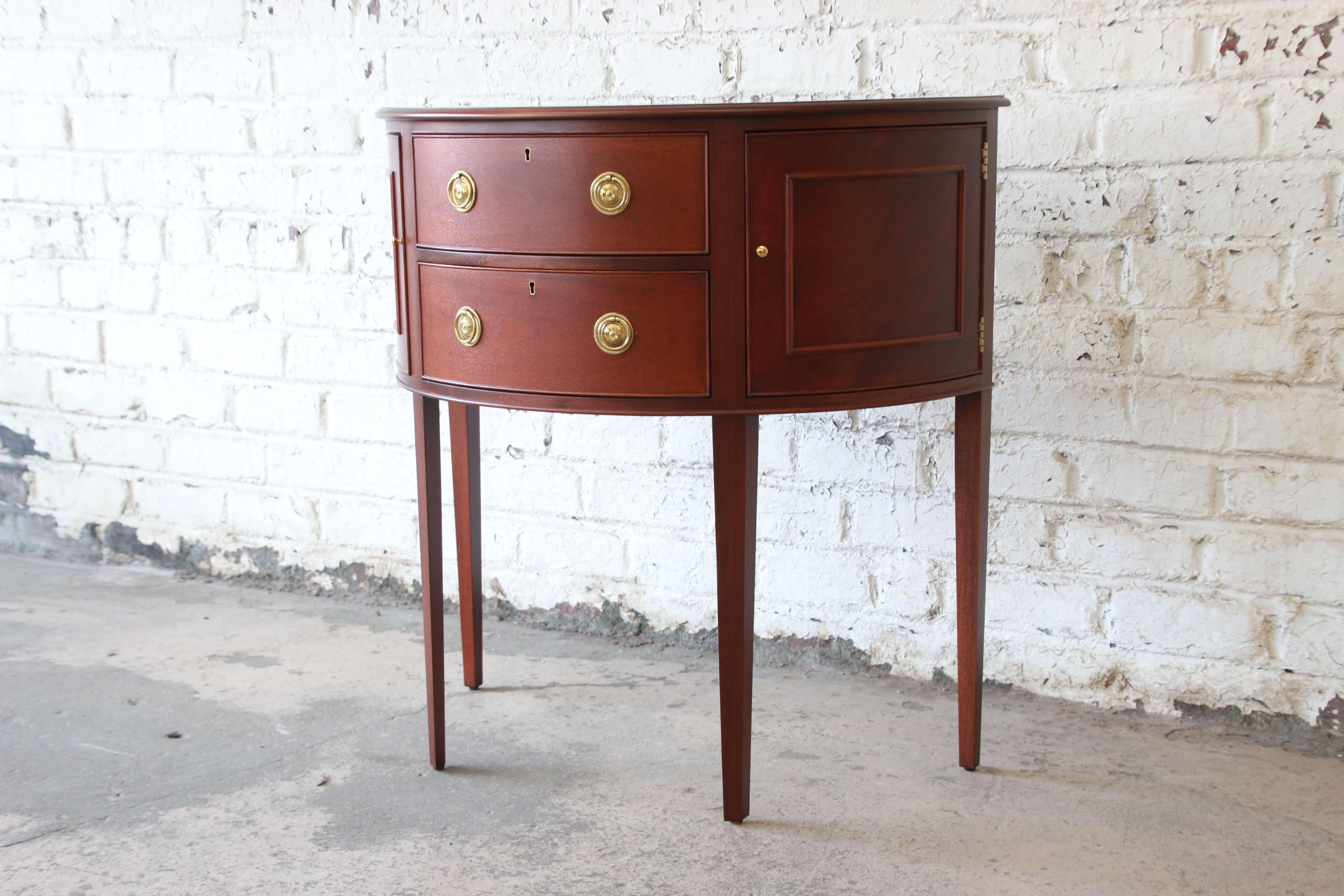 Offering a very nice mahogany demilune cabinet or sideboard by Baker Furniture. The piece has two large centre drawers that open and close smoothly with nice brass hardware. On each side of the drawers there are cabinet doors that open for