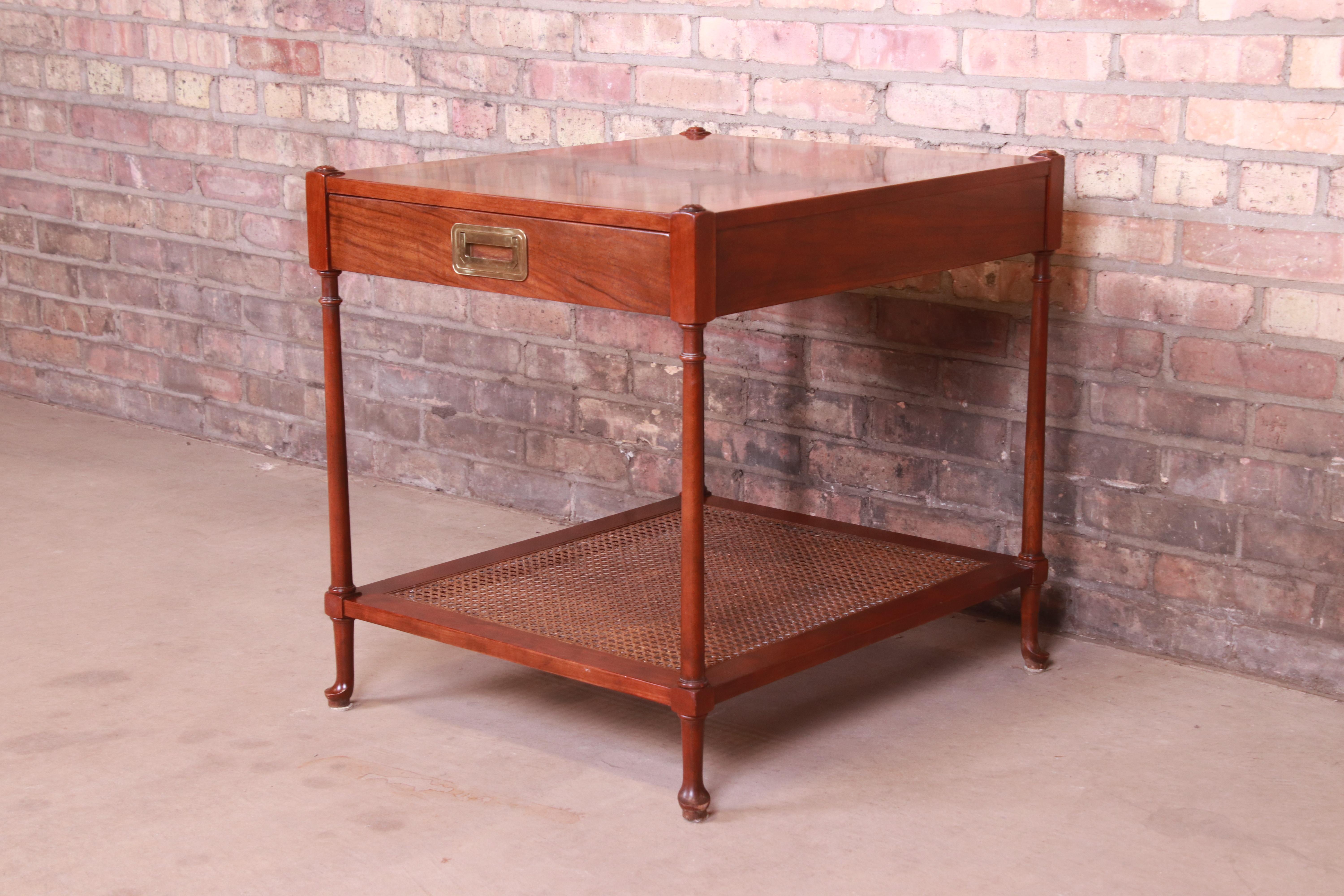 A gorgeous Mid-Century Modern Hollywood Regency Campaign style two-tier occasional side table or nightstand

By Baker Furniture

USA, Circa 1960s

Cherry wood, with burled walnut top, cane shelf, and original brass hardware.

Measures: 22
