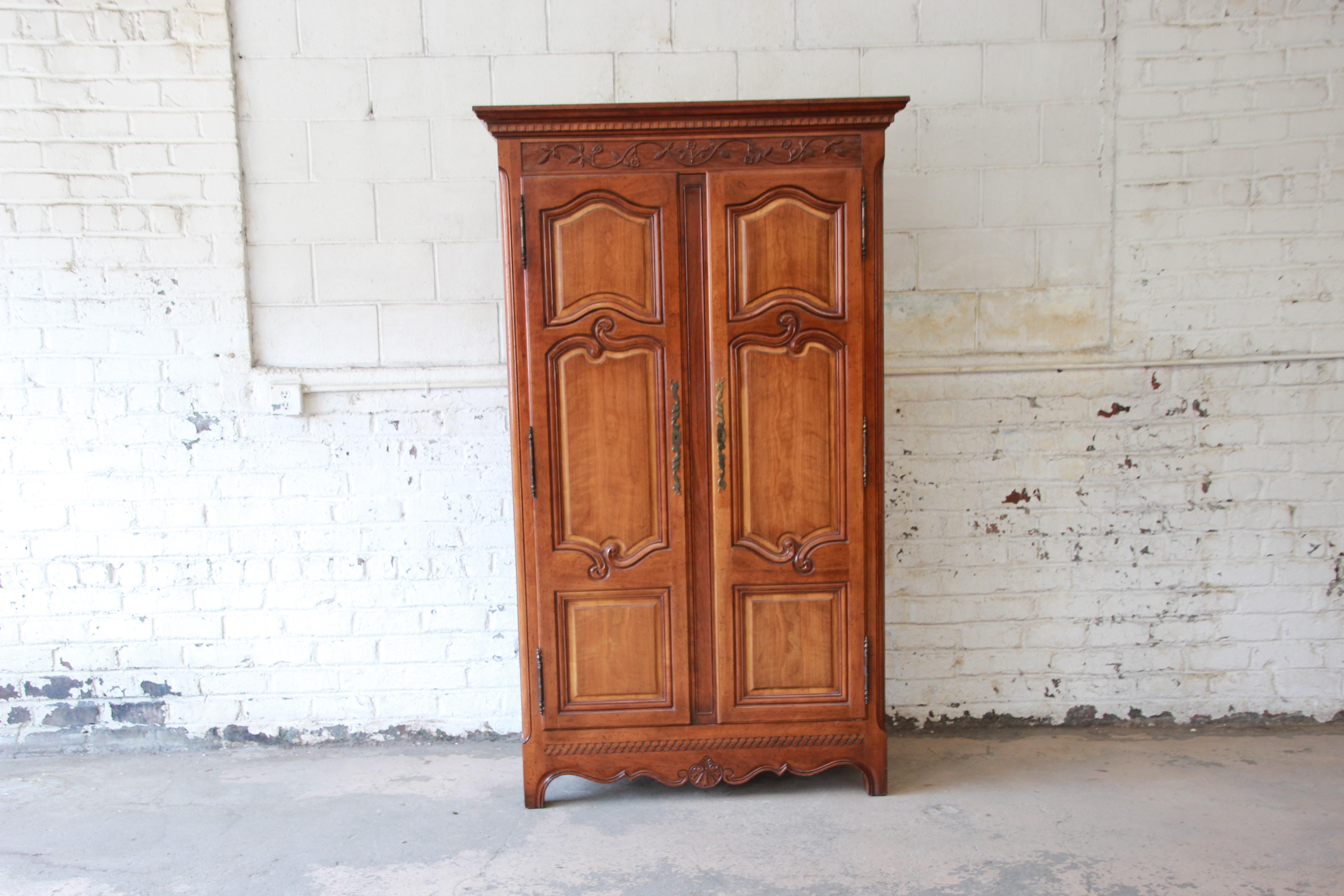 A gorgeous Country French cherry wood armoire or wardrobe dresser from the Milling Road Collection by Baker Furniture. The armoire features stunning wood grain and nice carved wood details. It offers ample room for storage, with four deep dovetailed
