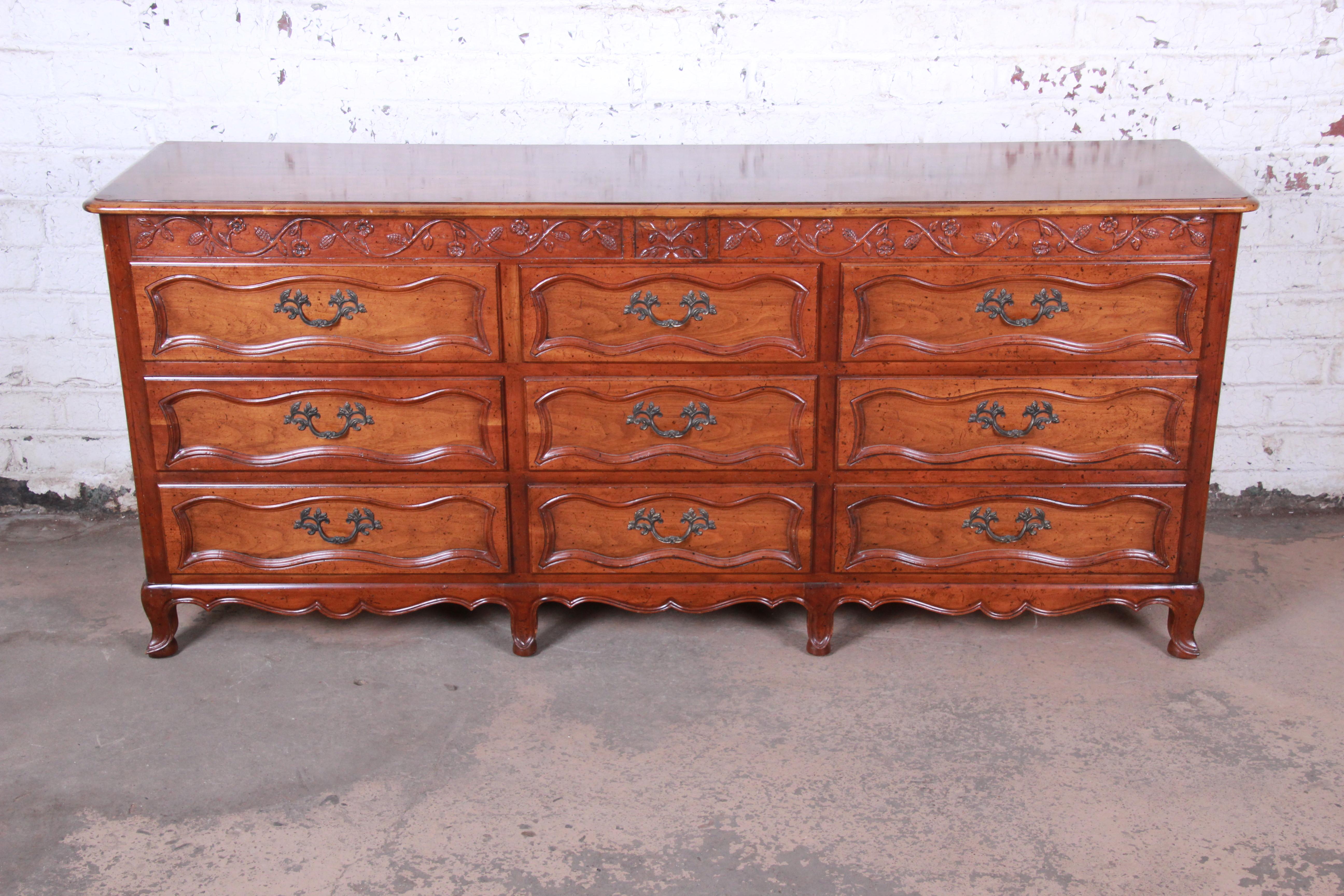 An exceptional French Provincial Louis XV style triple dresser or credenza from the Milling Road Collection by Baker Furniture. The dresser features gorgeous cherrywood grain with nice carved wood details. It offers ample storage, with nine deep