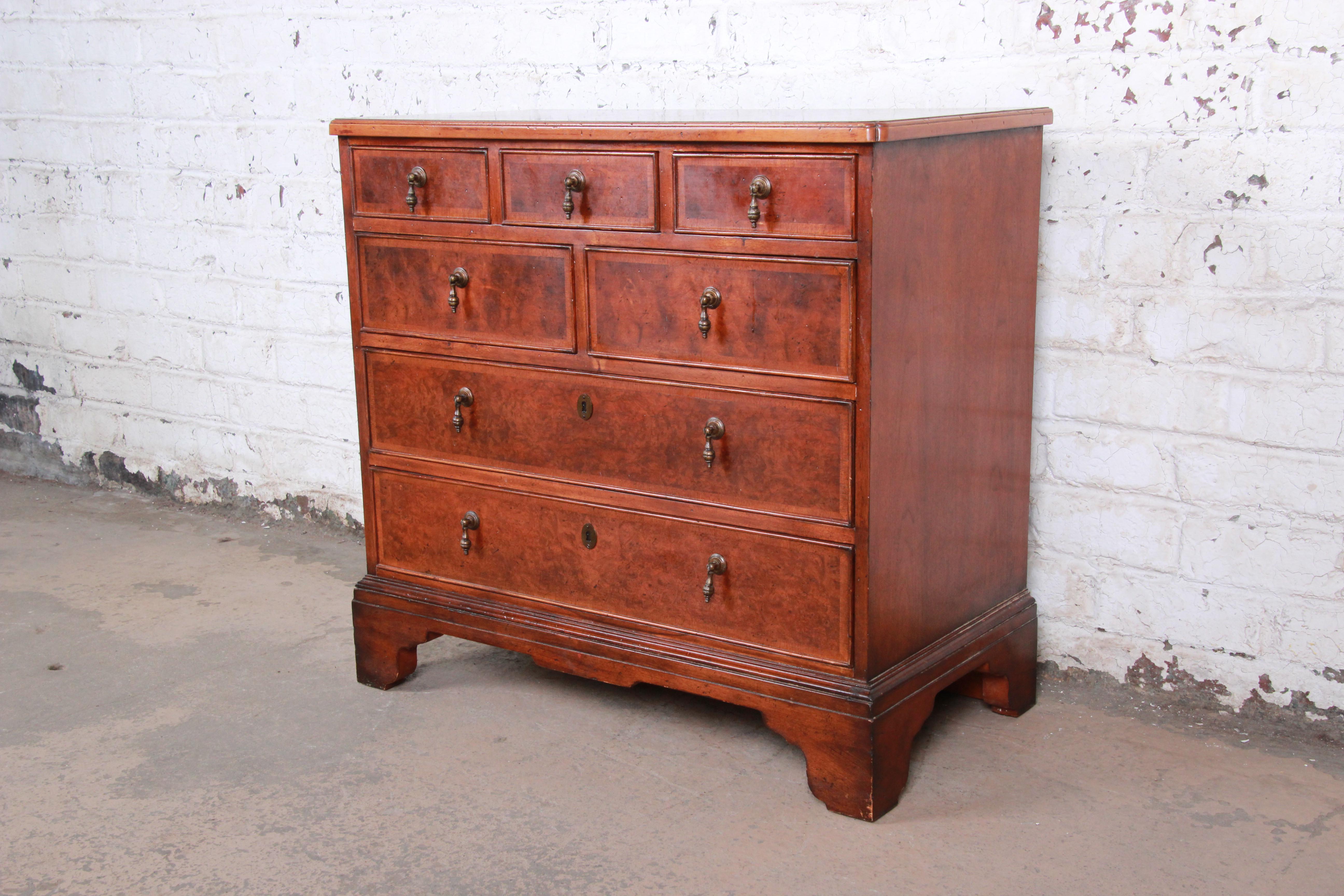 An exceptional Georgian burled walnut chest of drawers from the Milling Road line by Baker Furniture. The dresser features stunning burled walnut and banded mahogany wood grain and a nice traditional English style. It offers ample storage, with