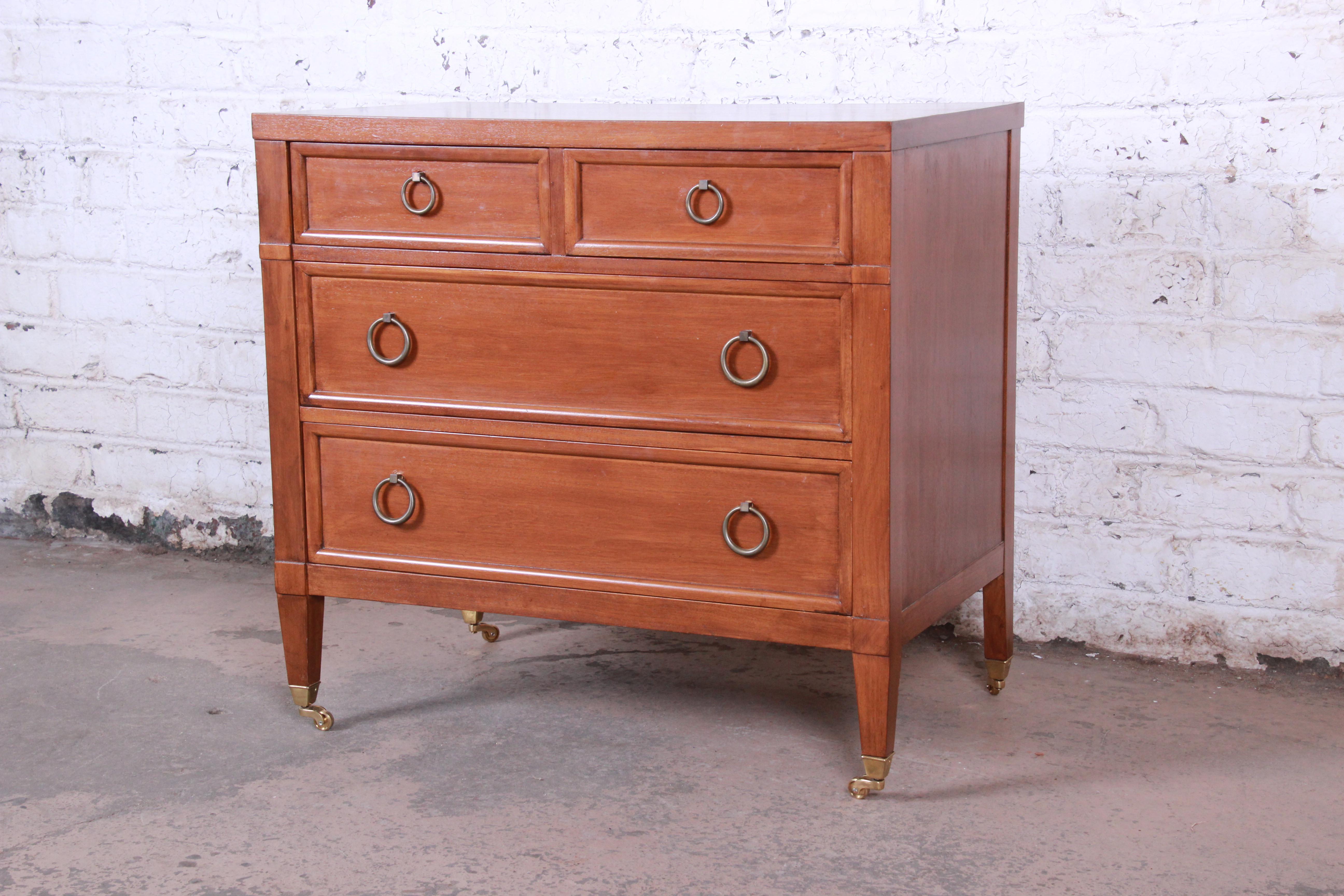 A gorgeous four-drawer midcentury bachelor chest dresser from the Milling Road line by Baker Furniture. The chest features beautiful wood grain and original brass ring drawer pulls, as well as original brass casters. It offers good storage, with