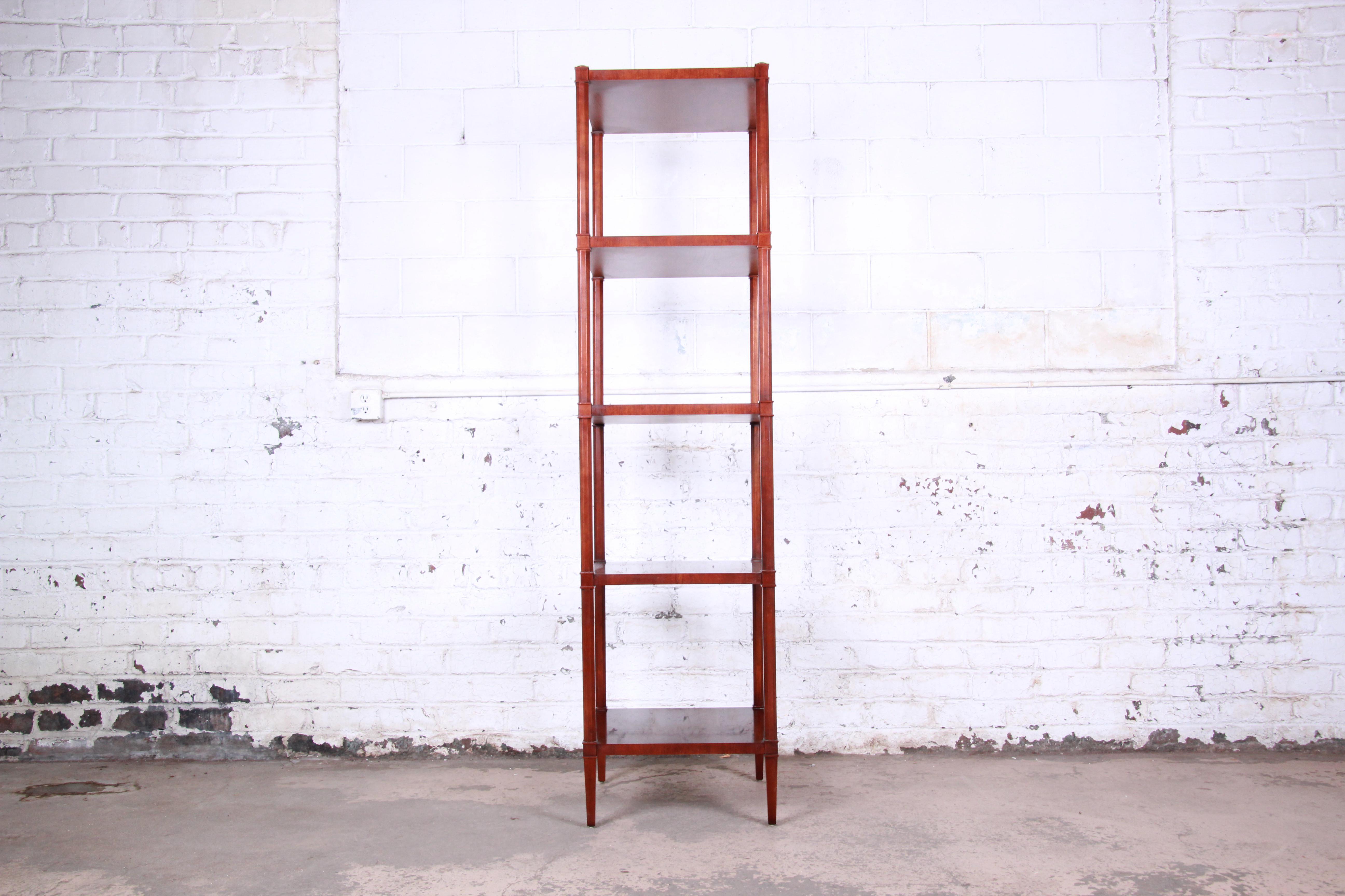 An exceptional Neoclassical style etagere by Baker Furniture. The etagere features beautiful mahogany wood grain, with brass accents and tapered legs. It offers excellent storage and display, with four open shelves. The original Baker label is