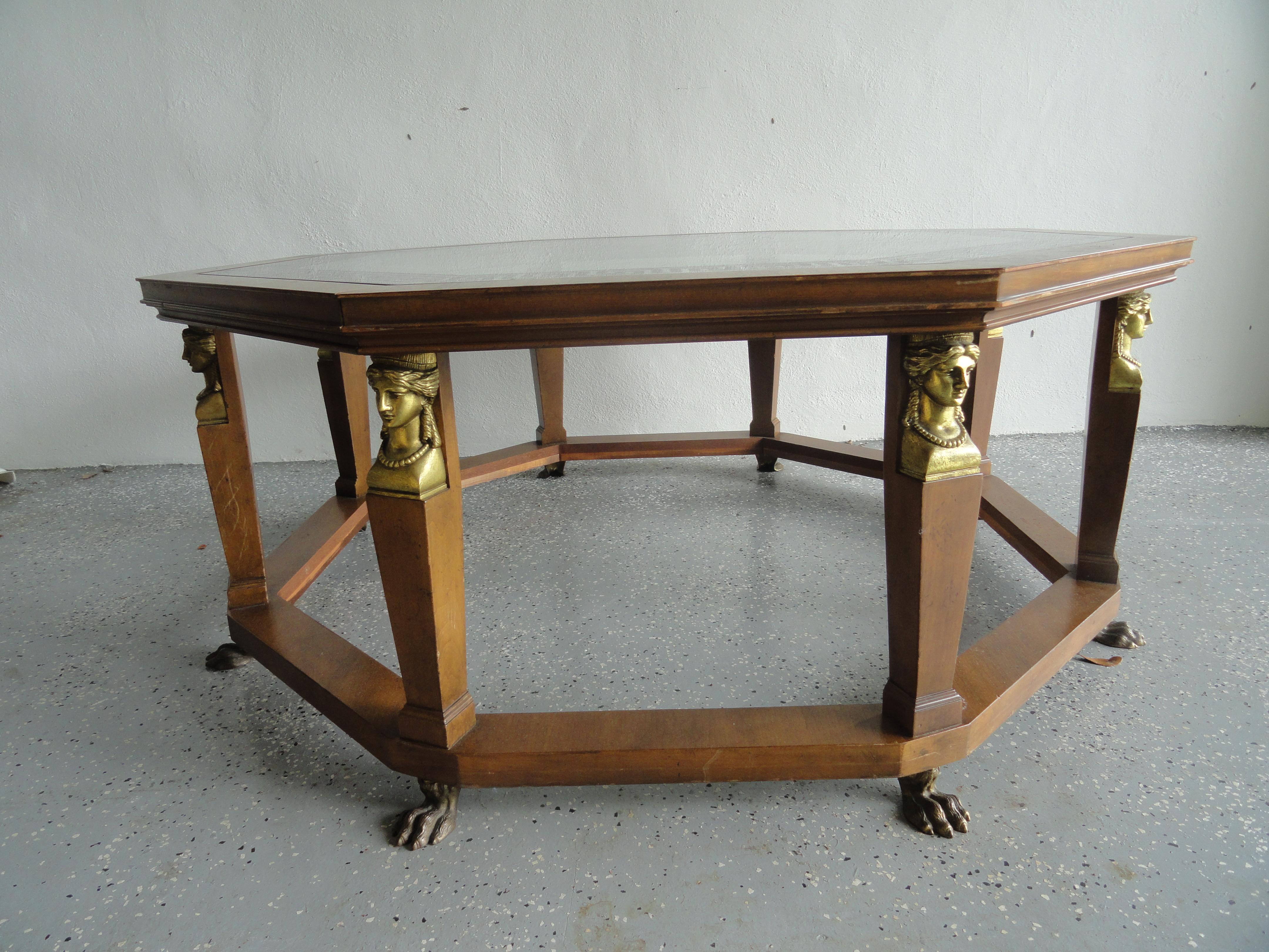 Octagonal coffee table from Baker Furniture. Octagonal glass top with Greek key border. Eight upright legs feature a brass claw and a brass caryatid supporting the top. Various woods, 1960s. Egyptian Revival.