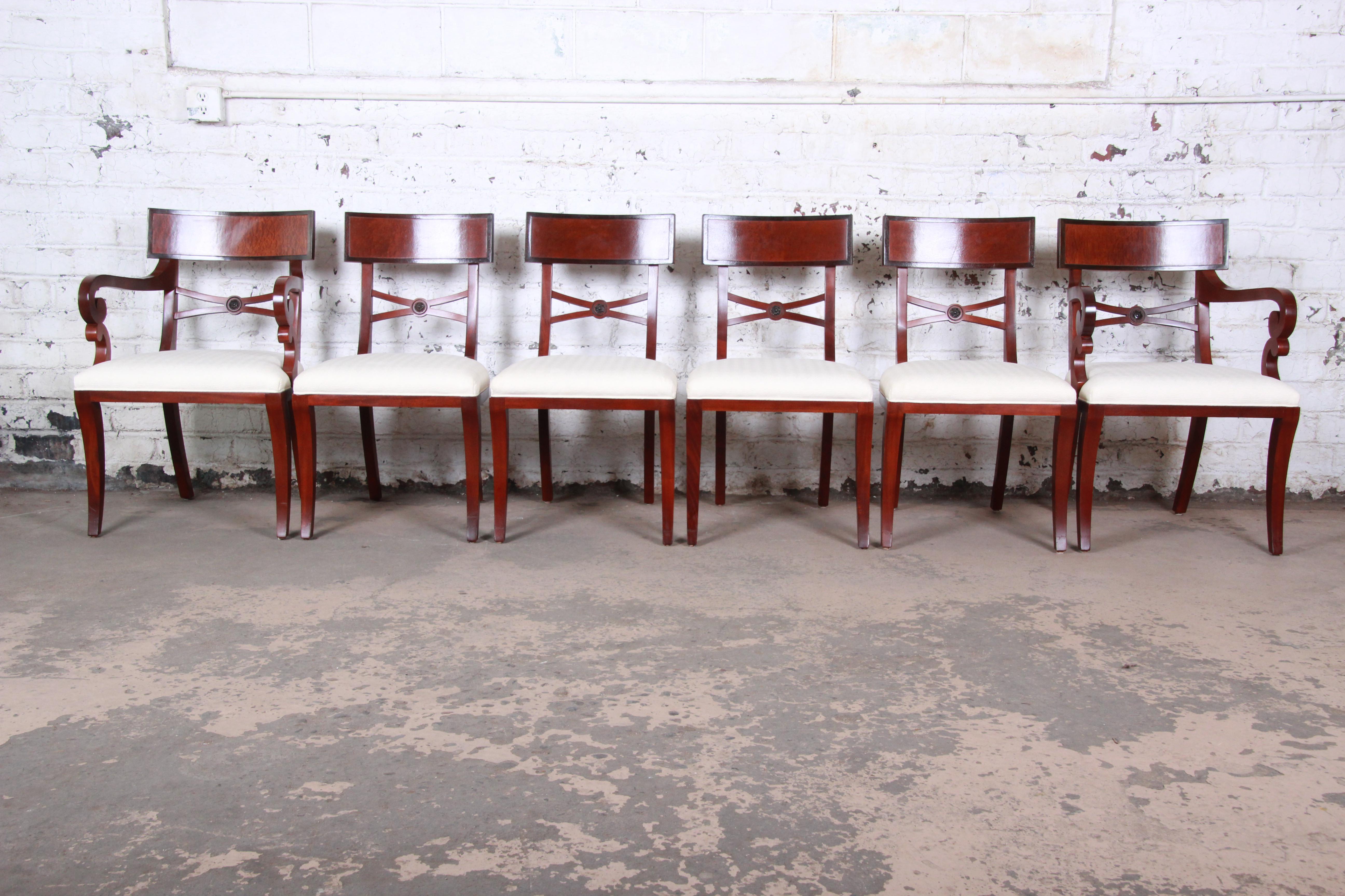 An exceptional set of Regency style mahogany dining chairs by Baker Furniture. The set includes two captain armchairs and four side chairs. The chairs feature solid mahogany construction and a nice traditional style. The ivory upholstery is in very