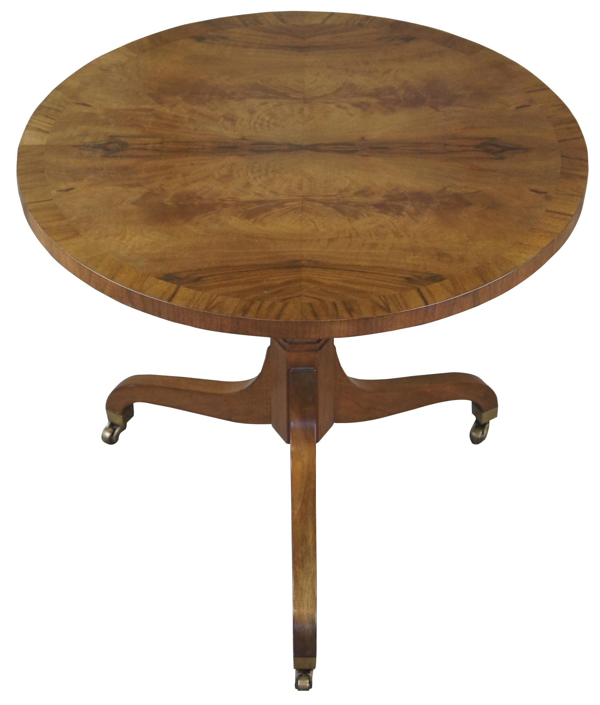 Baker Furniture Regency style side table, Circa 1970s. Made from walnut with a banded and bookmatched veneered top, supported by a hexagonal turned center support over tripod base with curved legs featuring brass caps and casters. Marked along