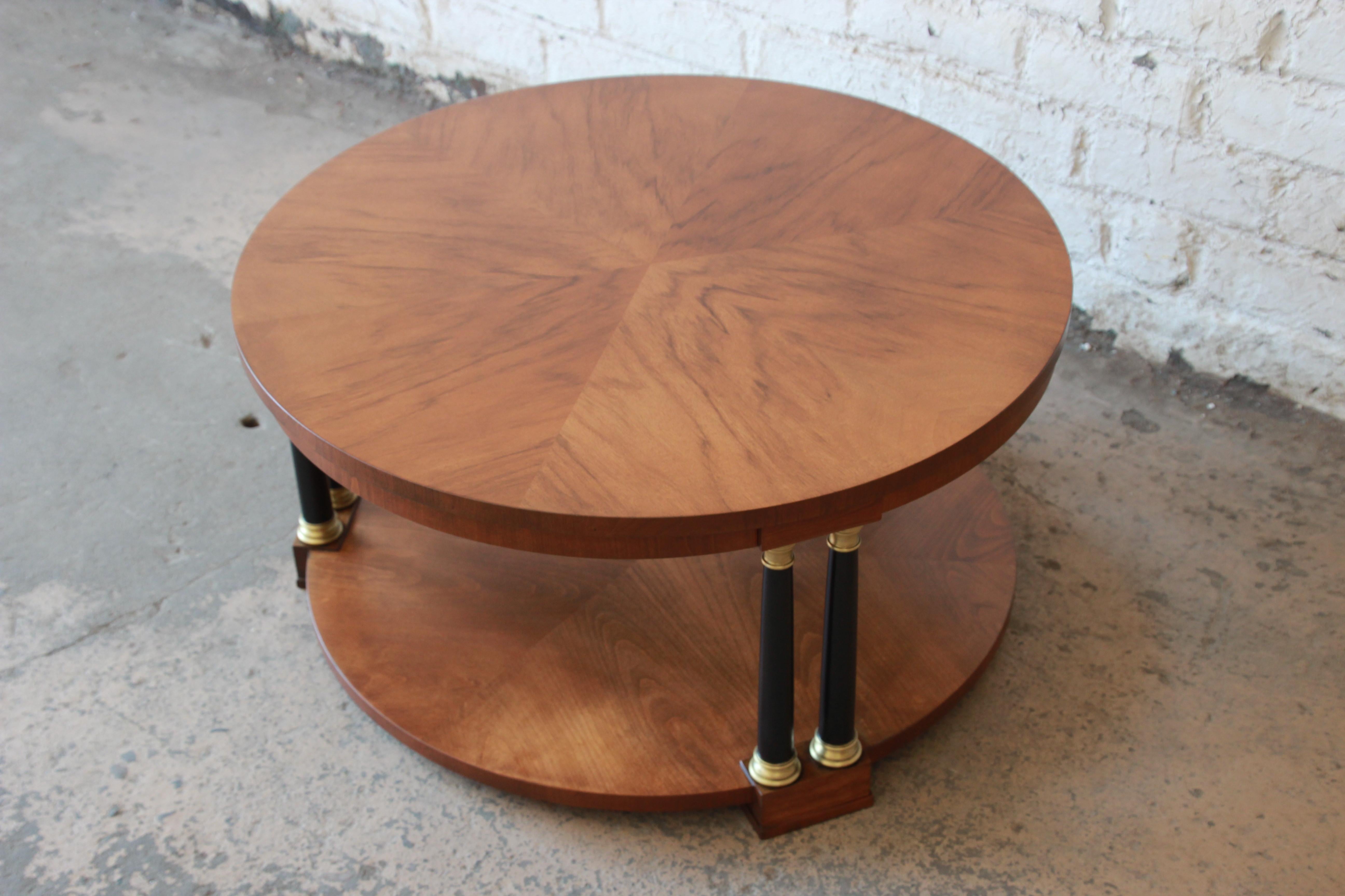 Offering a beautiful and rare round neoclassical coffee table by Baker Furniture Co. The table has a stunning wood grain with three sections of pairs of ebonized columns with solid brass details. The table is fitting for any elegant or traditional