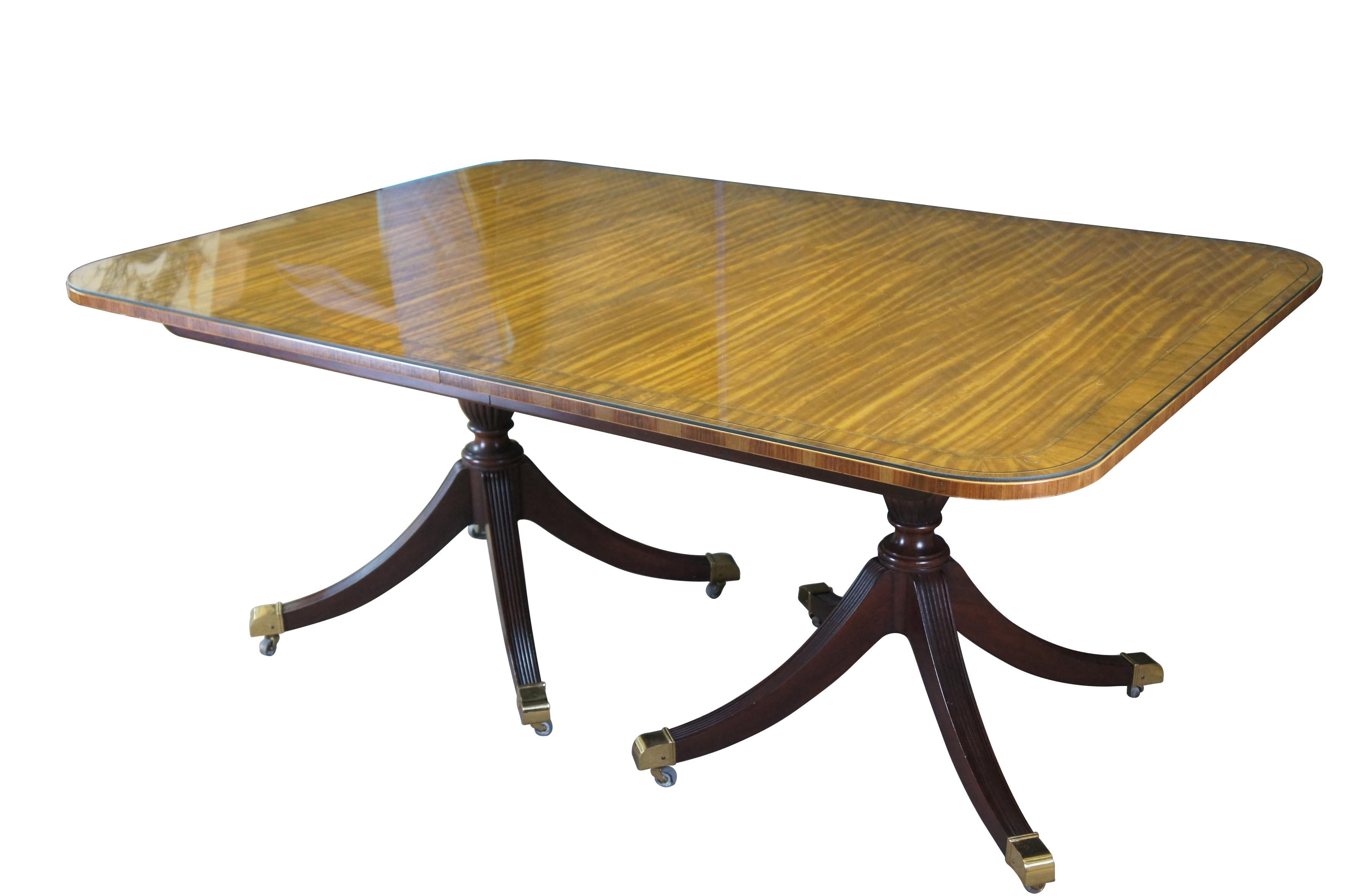 Baker Furniture Collector's Edition Duncan Phyfe dining table.  Features an impressive satinwood banded top with custom made protective glass covering.  The table is supported by a double pedestal mahogany base with shapely reeded urns over four