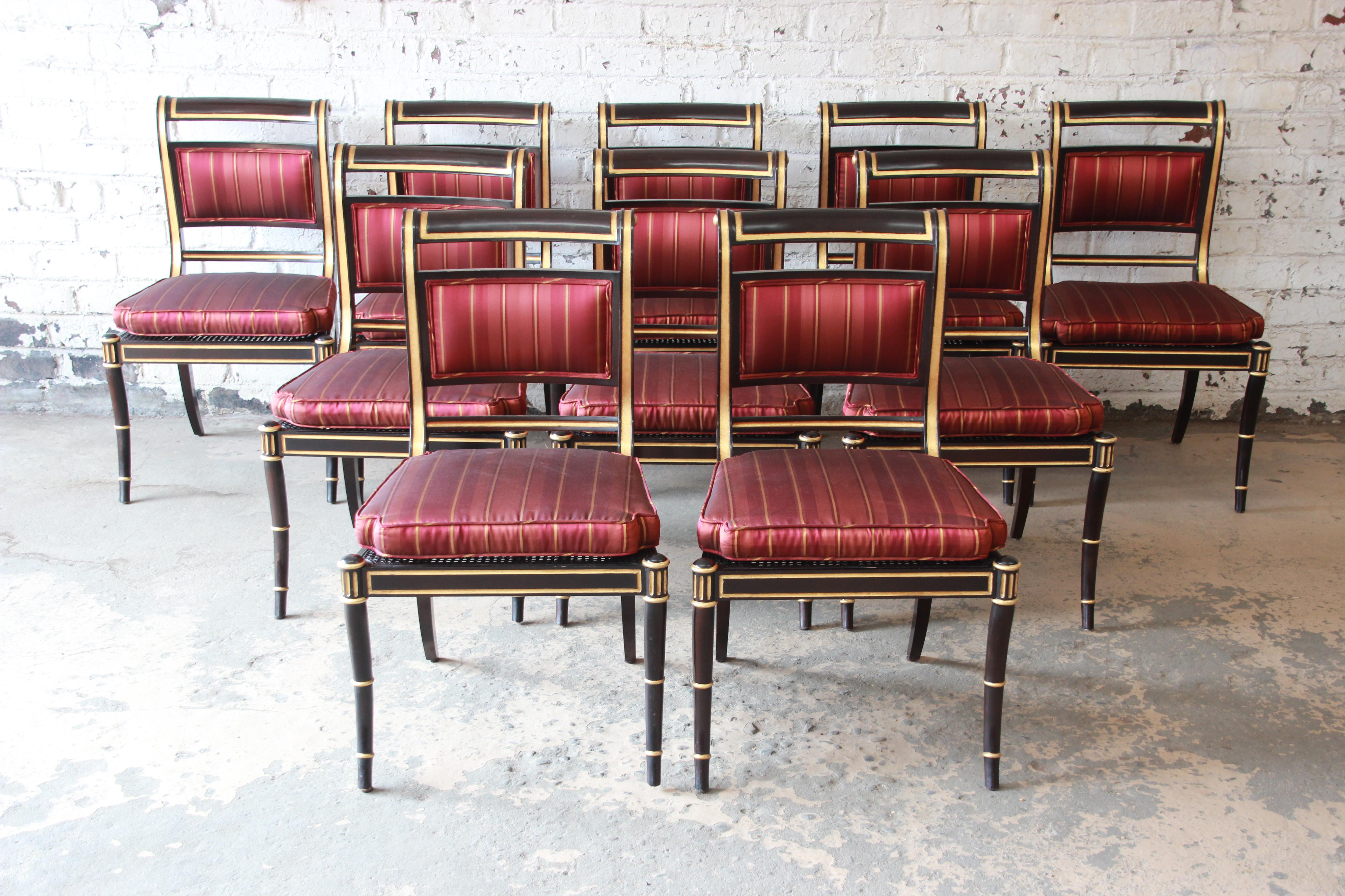 Offering a gorgeous set of ten Regency style dining chairs from the Baker Furniture Stately Homes Collection. The chairs feature a black finish with gold accents, caned backs and seats. Included are the original red and gold seat cushions. A