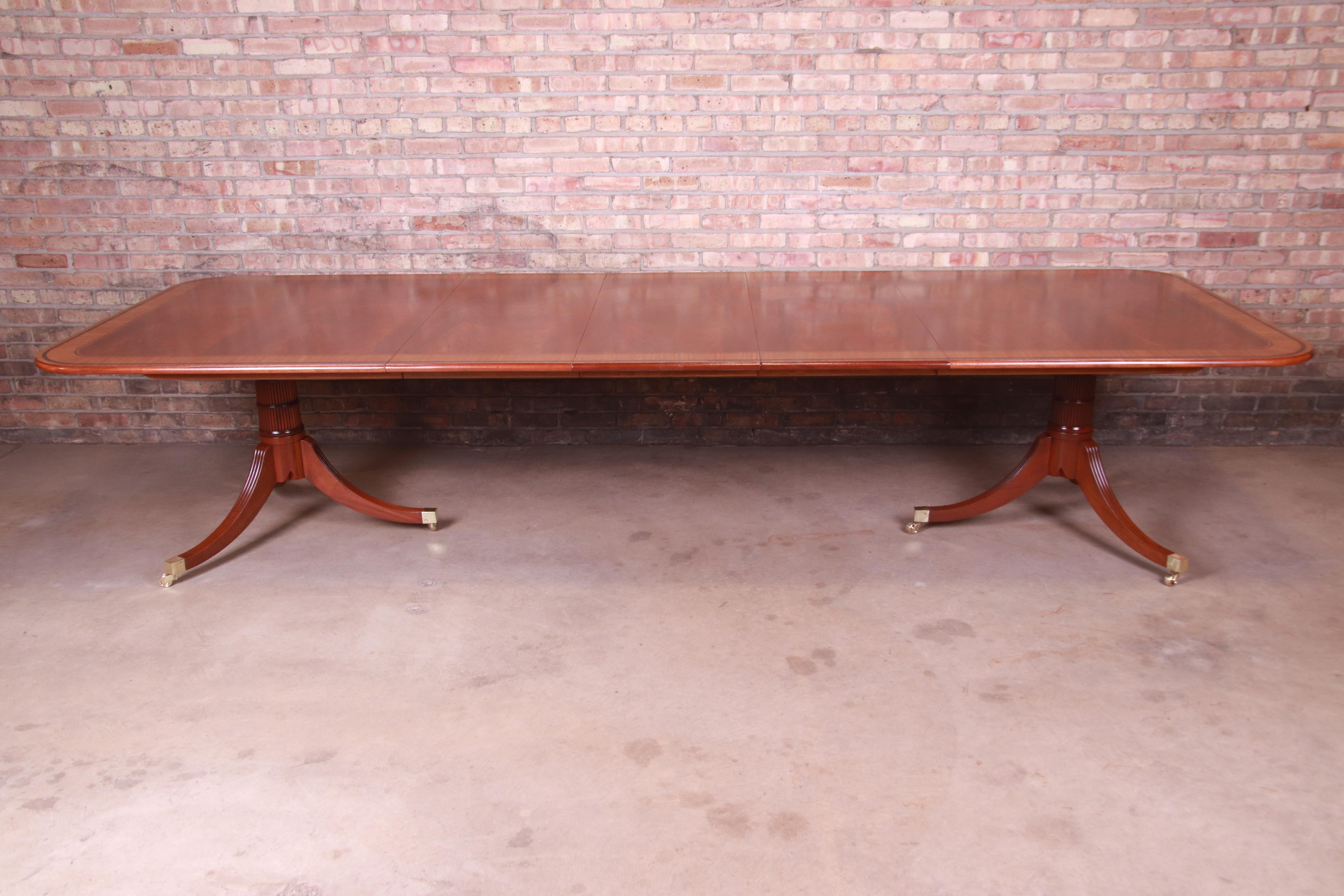 A rare and truly exceptional mahogany and satinwood extension dining table from Baker Furniture's Stately Homes Collection. This fine Regency table is a two-pedestal mahogany table with broad satinwood crossbanded and ebonized borders and a rounded