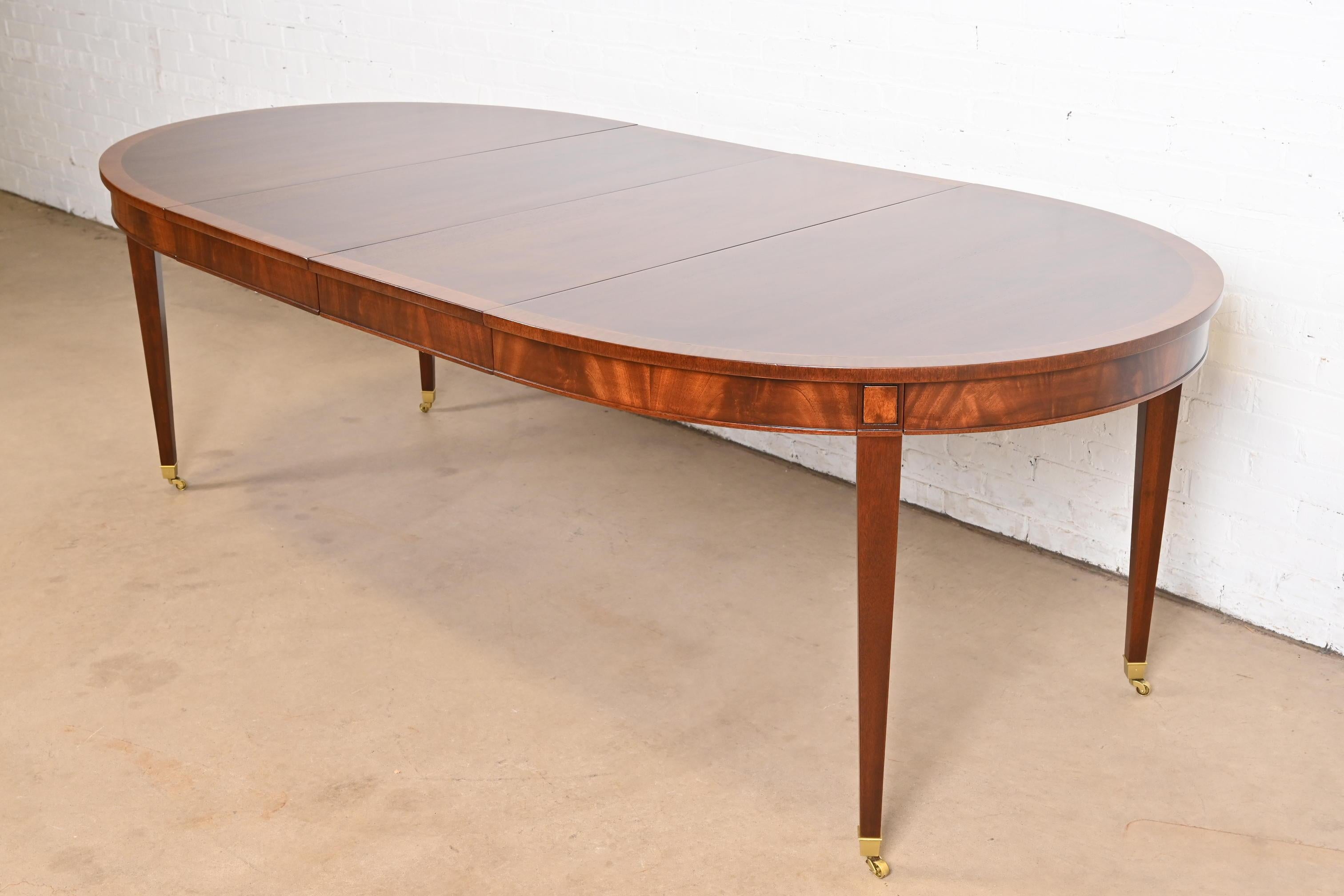 A gorgeous Federal or Hepplewhite style extension dining table

In the manner of Baker Furniture

USA, Circa 1960s

Gorgeous book-matched mahogany, with satinwood banding, flame mahogany apron, and brass-capped feet on brass casters.

Measures: 58