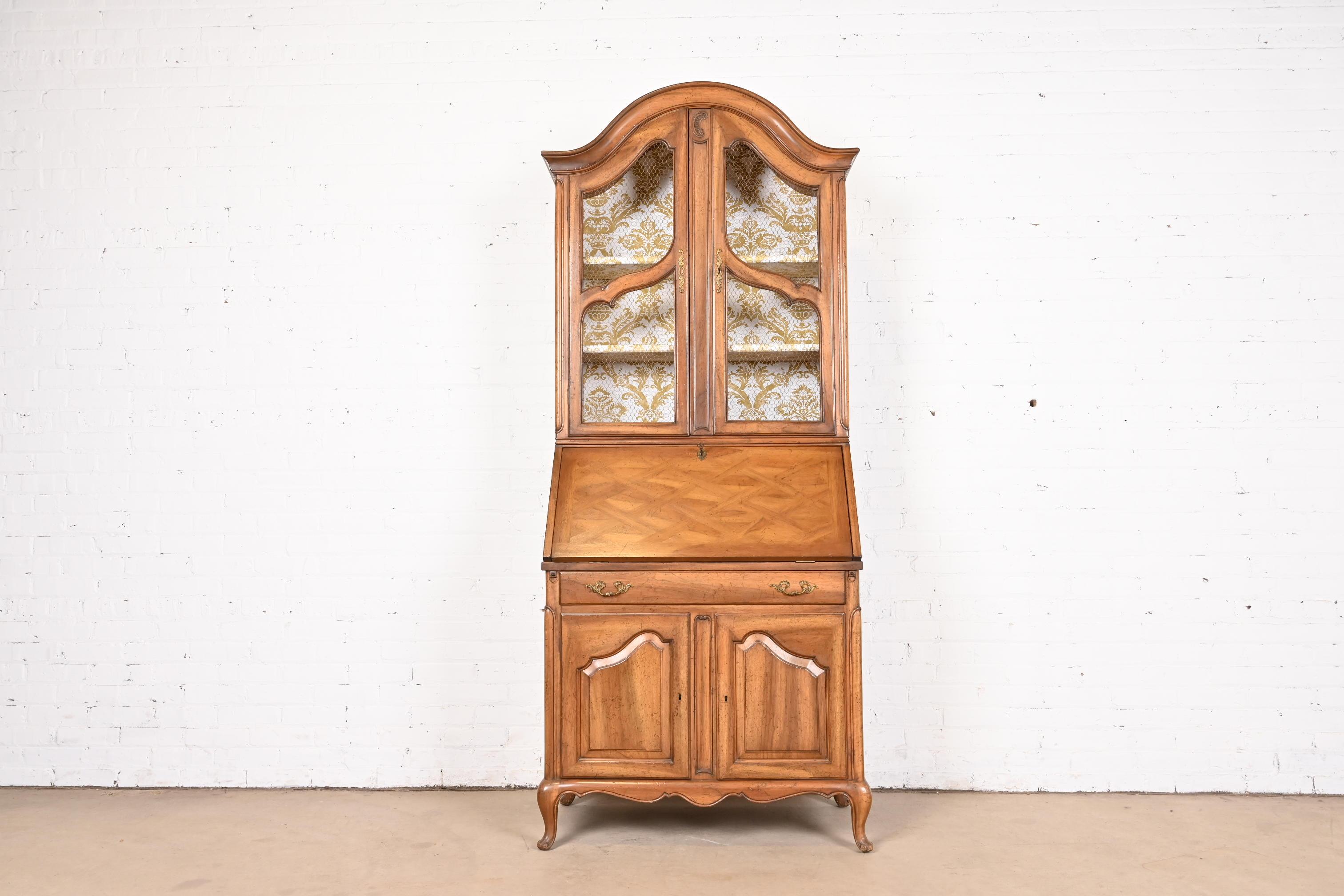 A gorgeous French Provincial Louis XV style bureau with drop front secretary desk and bookcase hutch top

In the manner of Baker Furniture

USA, Circa 1960s

Carved walnut, with original brass hardware, and embossed leather writing surface. Cabinet