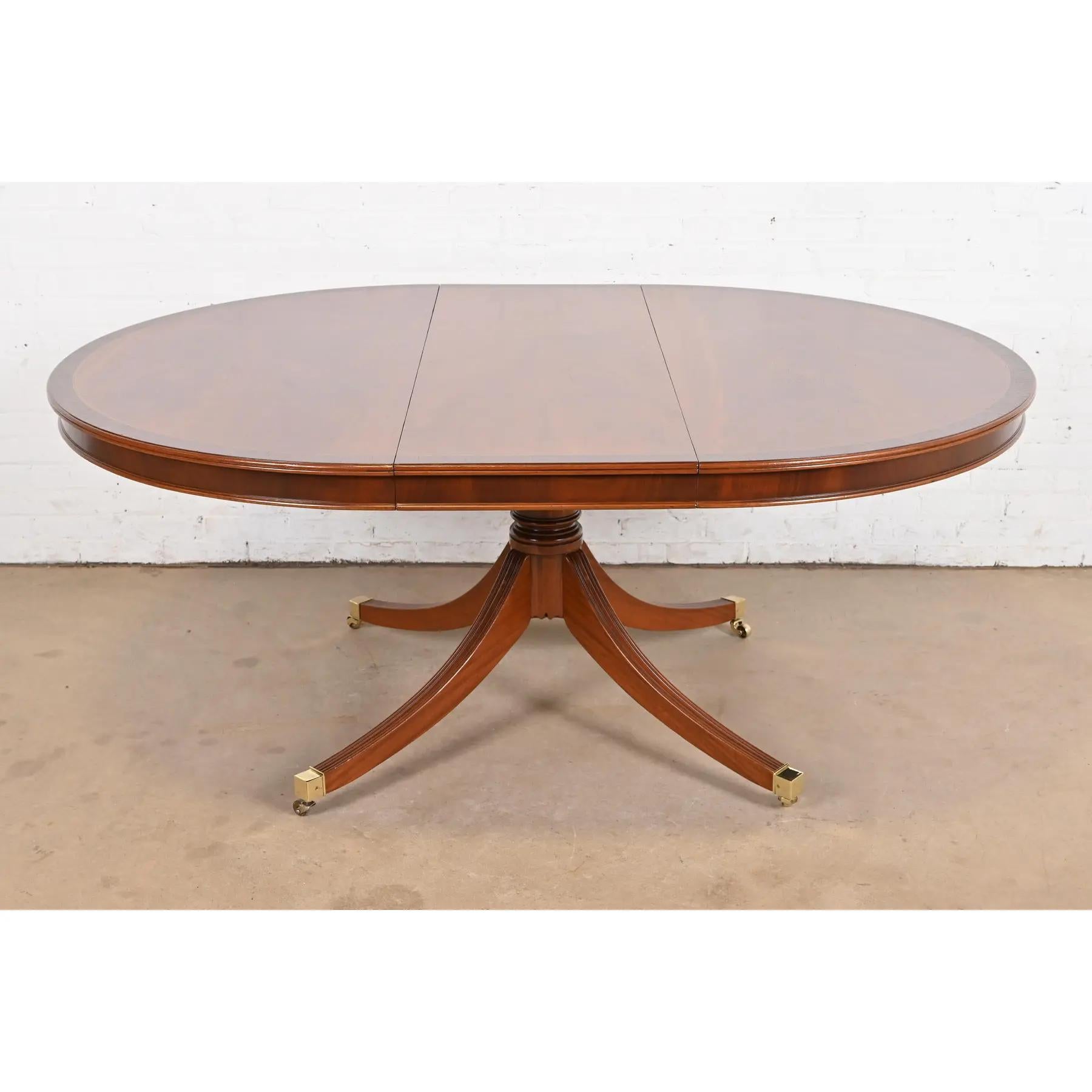 Ein außergewöhnlicher Esstisch im georgianischen oder Regency-Stil mit ausziehbarem Sockel

Nach dem Vorbild von Baker Furniture

USA, ca. 1980er Jahre

Wunderschöne Mahagoni-Platte mit Palisanderbordüre, geschnitzter Sockel aus massivem Mahagoni