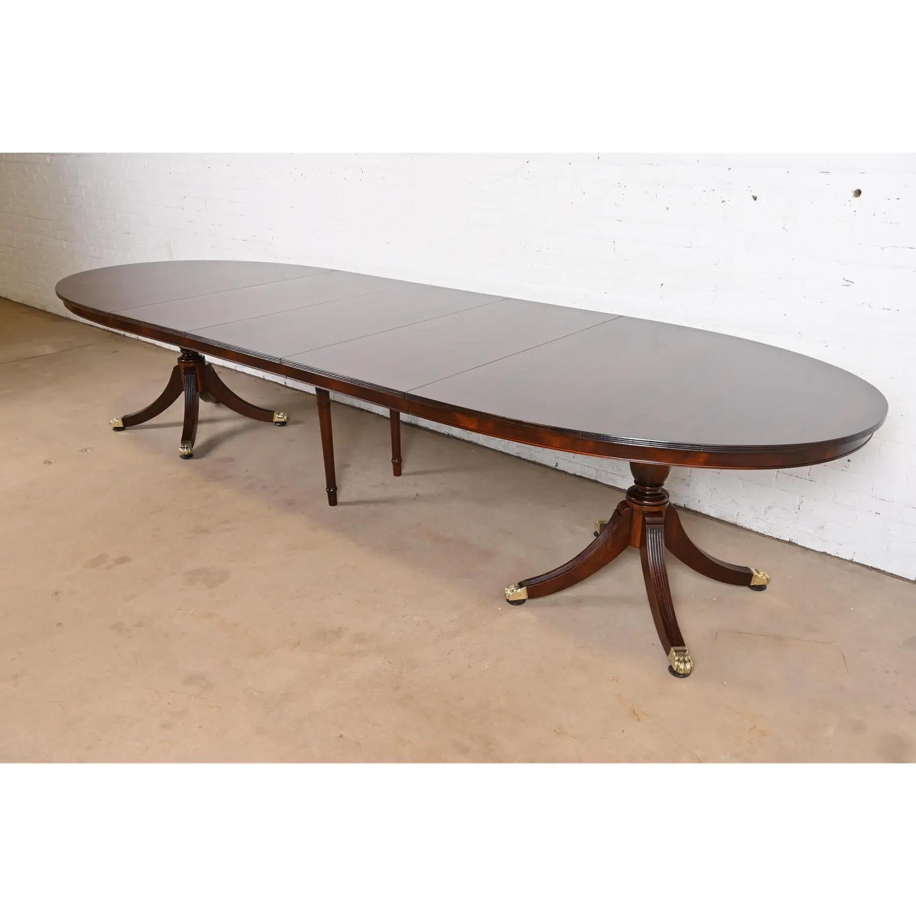 An exceptional Georgian or Regency style double pedestal extension dining table

In the manner of Baker Furniture

USA, Mid-20th Century

Gorgeous book-matched banded mahogany top, with carved solid mahogany pedestals, and brass-capped paw
