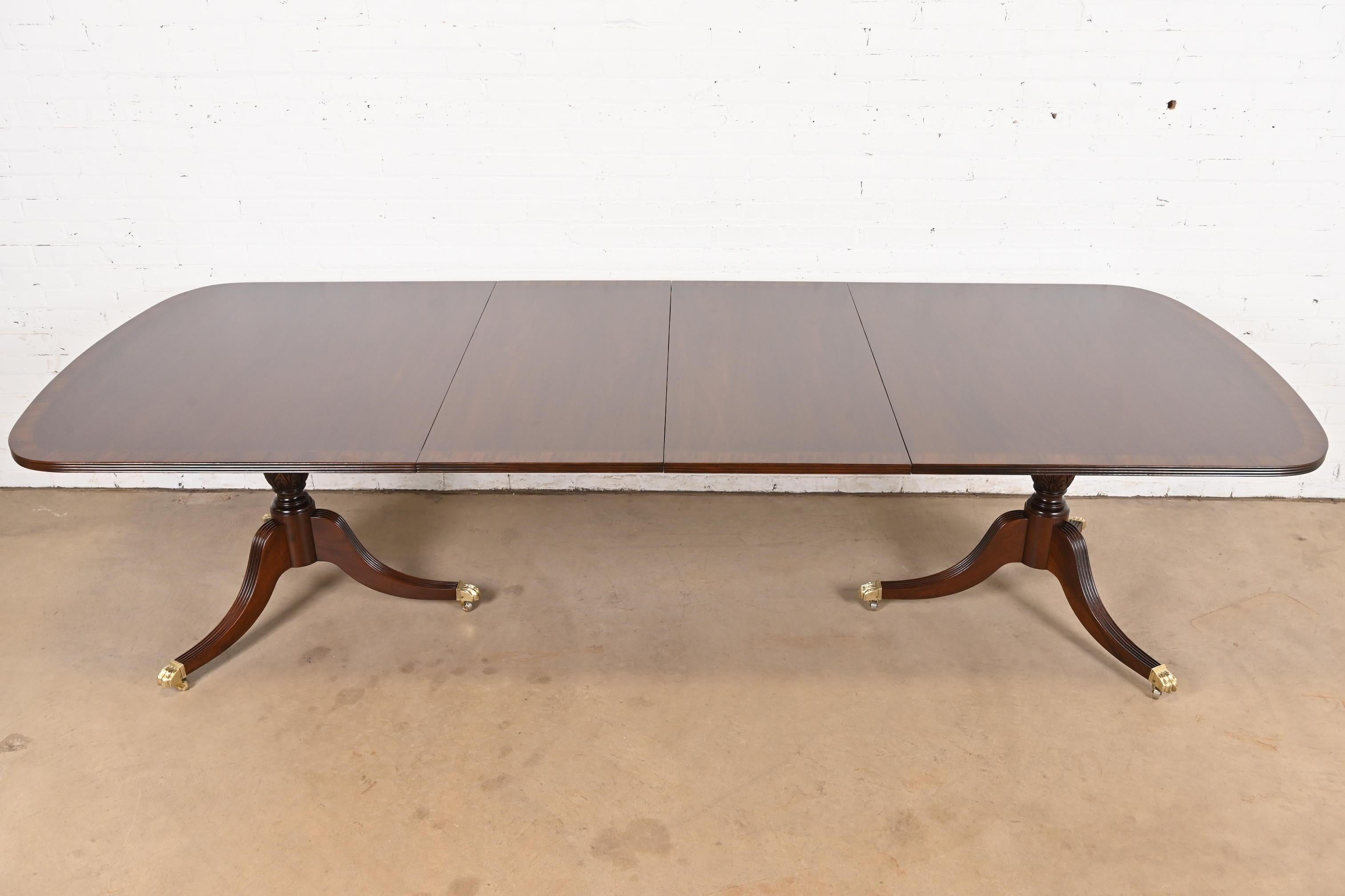 An exceptional Georgian or Regency style double pedestal extension dining table

In the manner of Baker Furniture

USA, Circa 1980s

Gorgeous mahogany, with satinwood banding, carved solid mahogany pedestals, and brass paw feet on brass