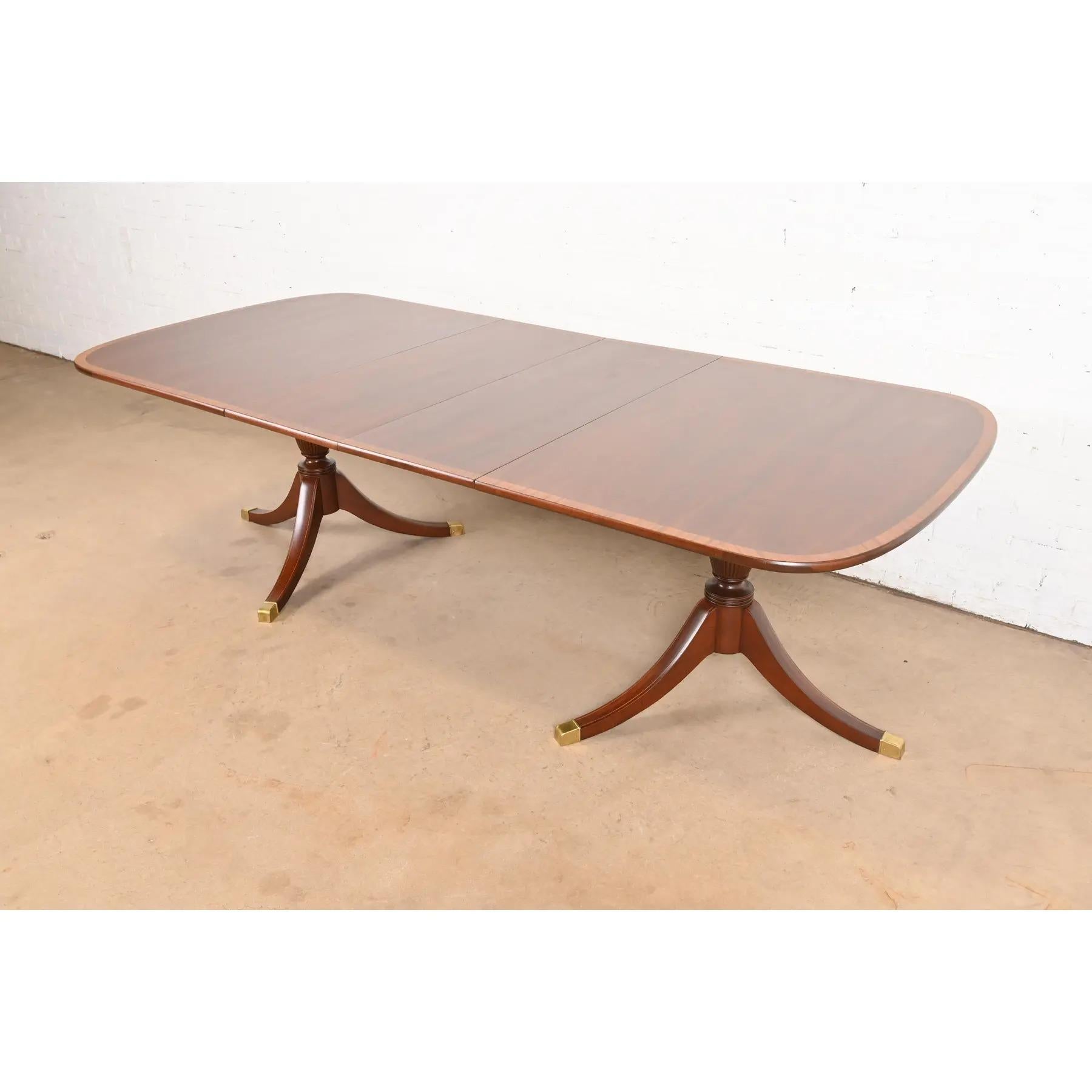 An exceptional Georgian or Regency style double pedestal extension dining table

In the manner of Baker Furniture

USA, Circa 1980s

Gorgeous mahogany, with satinwood banding, carved solid mahogany pedestals, and brass-capped feet.

Measures: 64