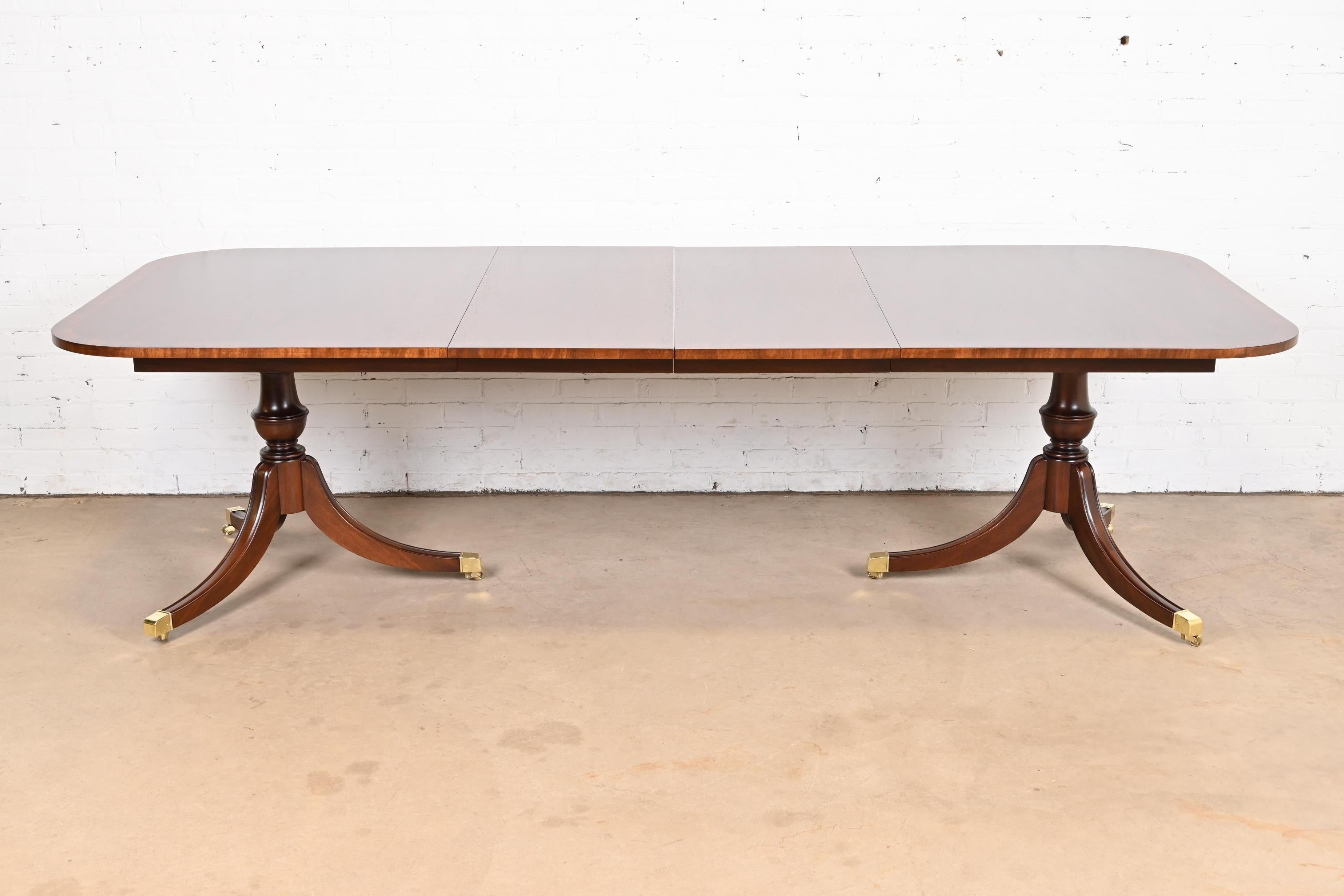 An exceptional Georgian or Regency style double pedestal extension dining table

In the manner of Baker Furniture

USA, Circa 1980s

Gorgeous banded mahogany top, with carved solid mahogany pedestals, and brass capped feet on brass
