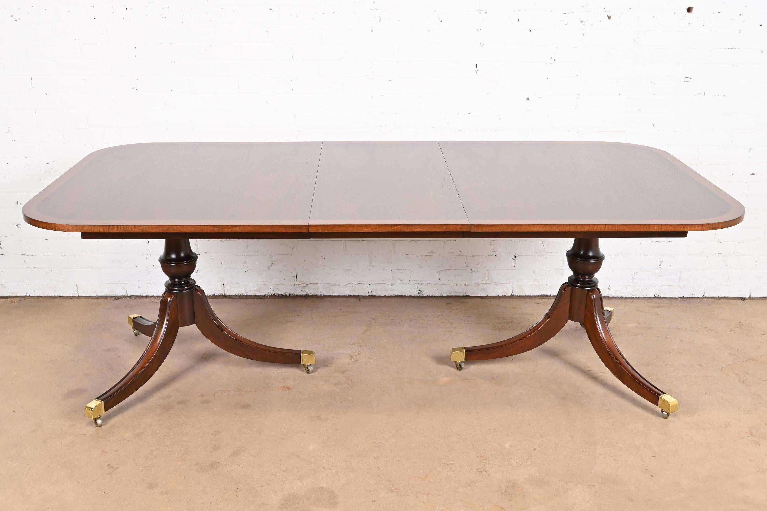 Exceptionnelle table à manger à rallonge à double piédestal de style Géorgien ou Régence.

À la manière des meubles Baker

USA, Circa 1980

Magnifique plateau en acajou assorti aux livres, avec bandes de bois satiné, piédestaux en acajou massif