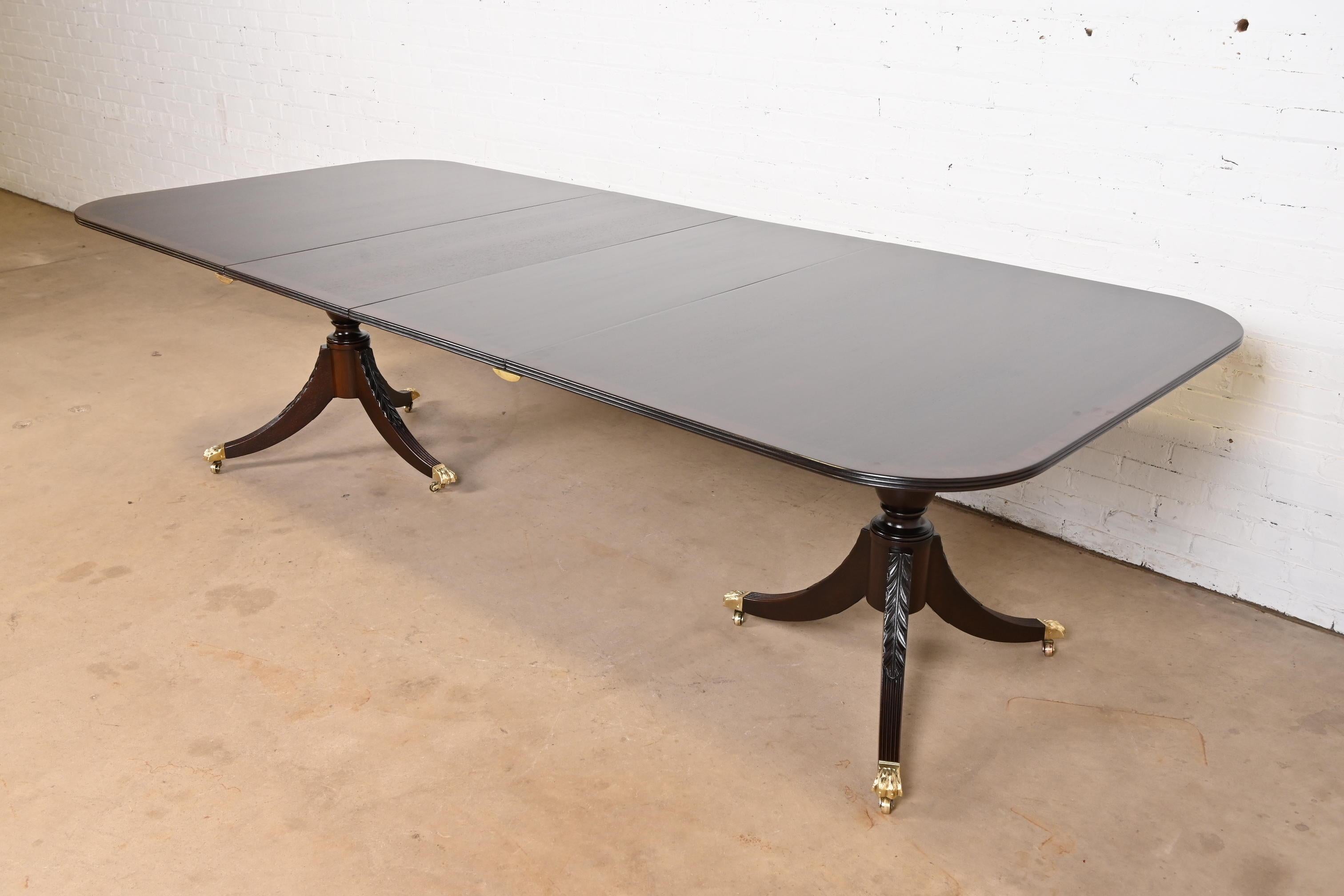 Exceptionnelle table à manger à rallonge à double piédestal de style Géorgien ou Régence.

À la manière des meubles Baker

États-Unis, fin du 20e siècle

Magnifique plateau d'acajou bagué, piédestaux en acajou massif sculpté et pieds en pattes de