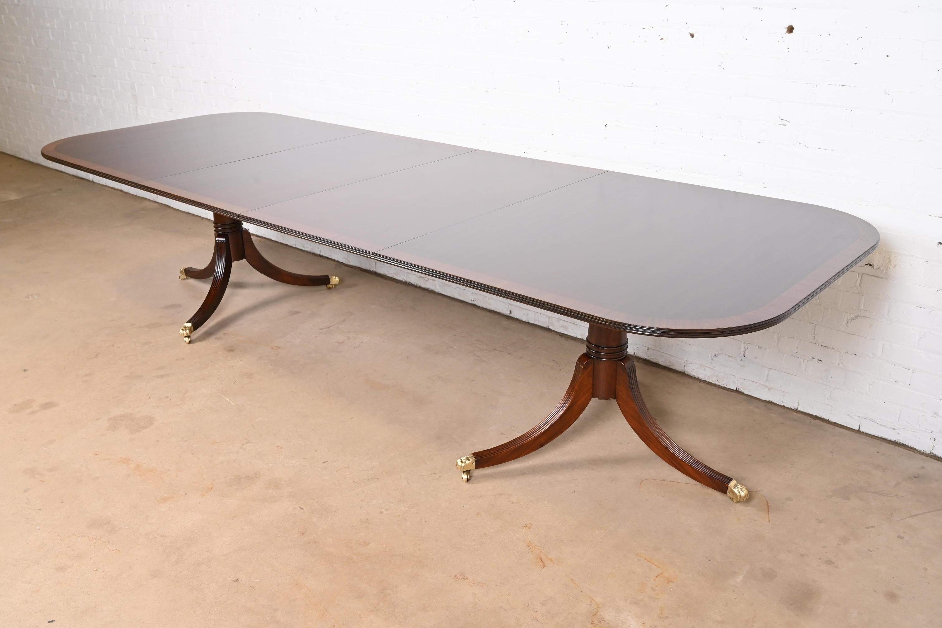 Exceptionnelle table à manger à rallonge à double piédestal de style Géorgien ou Régence.

À la manière des meubles Baker

USA, Circa 1980

Magnifique acajou, avec bandes de bois satiné, piédestaux en acajou massif sculpté, et pieds en patte d'oie