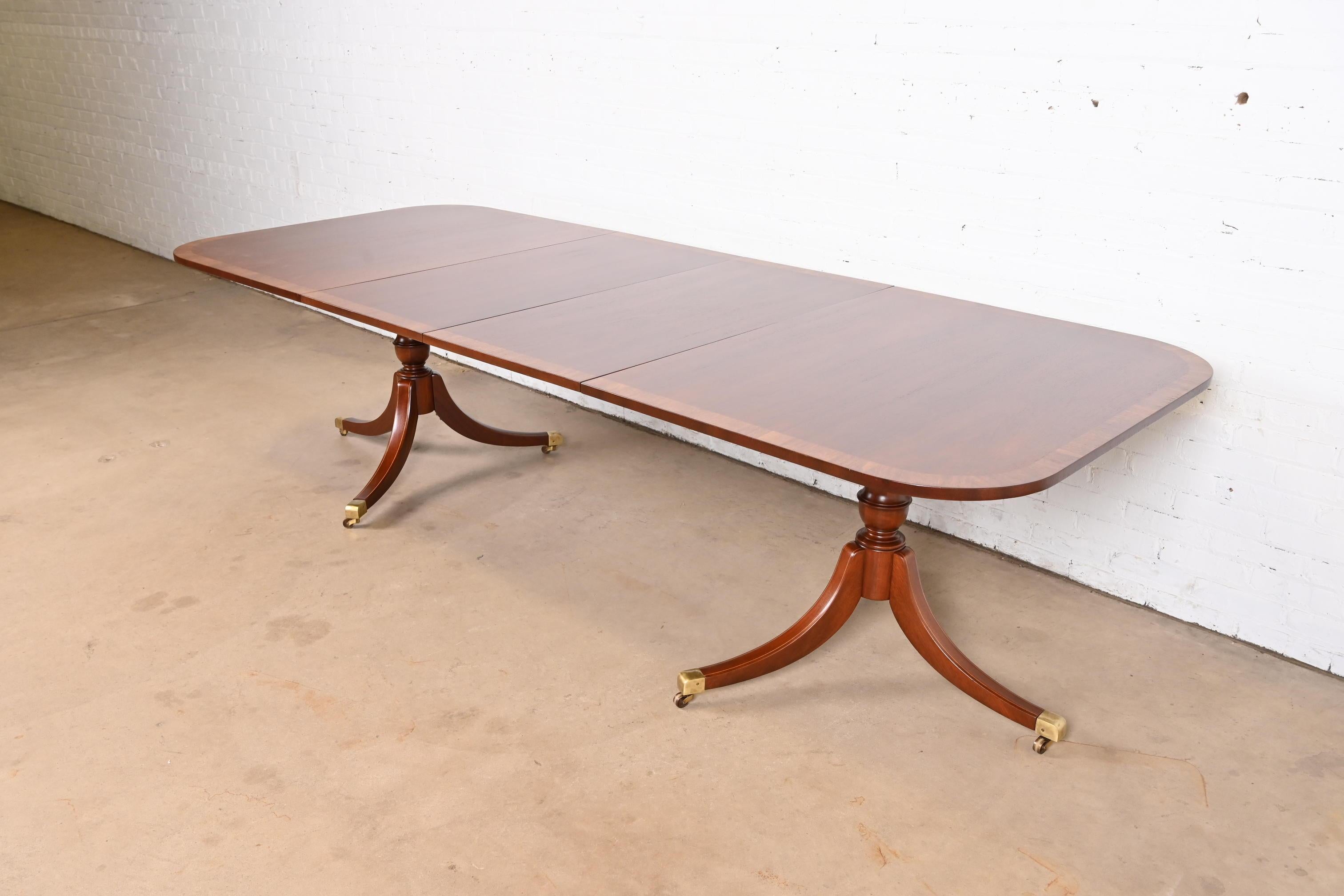 Exceptionnelle table à manger à rallonge à double piédestal de style Géorgien ou Régence.

À la manière des meubles Baker

USA, Circa 1980

Magnifique plateau en acajou bagué, piédestaux en acajou massif sculpté avec incrustation de cordes en bois