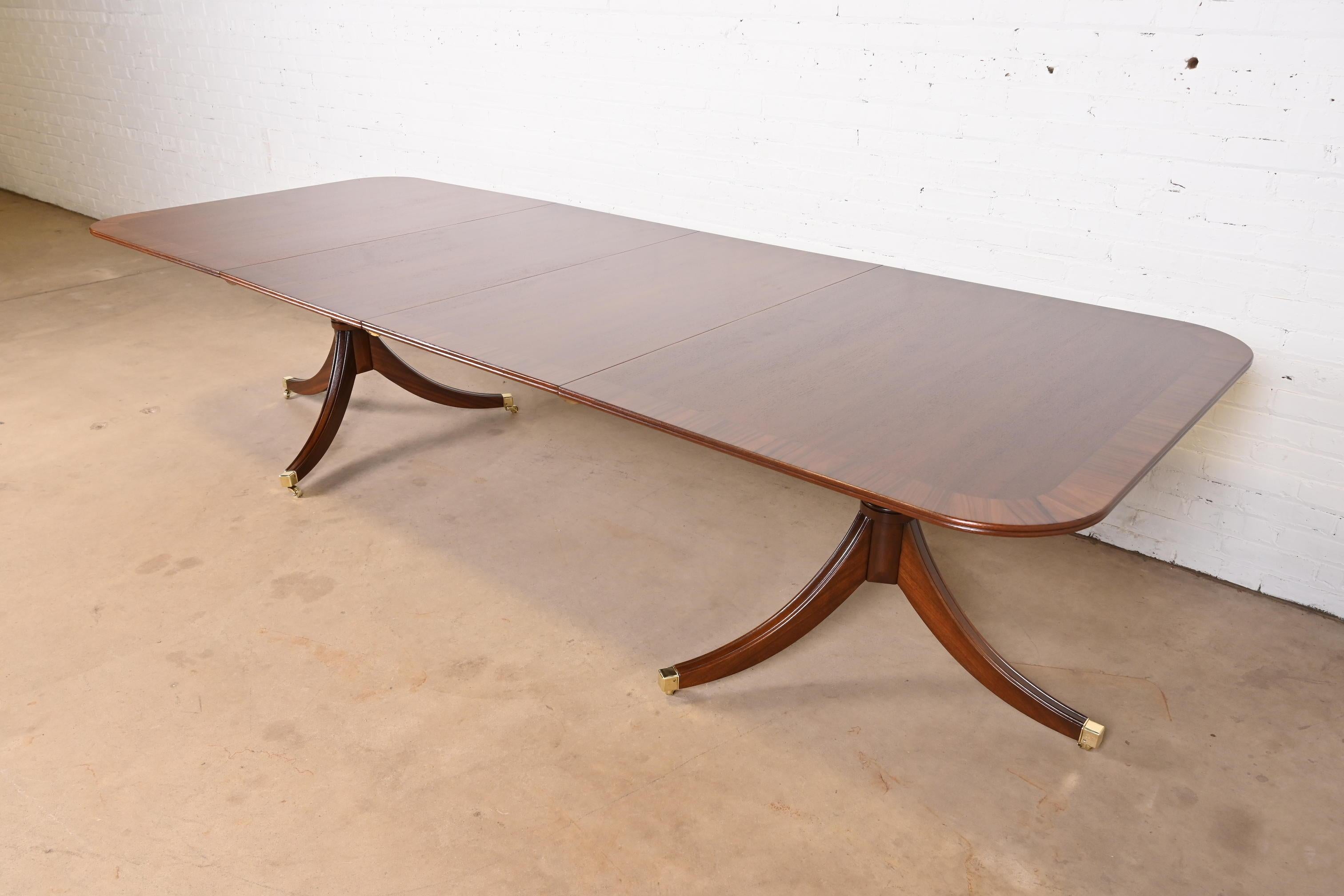 An exceptional Georgian or Regency style double pedestal extension dining table

In the manner of Baker Furniture

USA, Circa Mid-20th Century

Gorgeous mahogany, with rosewood banding, carved solid mahogany pedestals, and brass-capped feet on brass