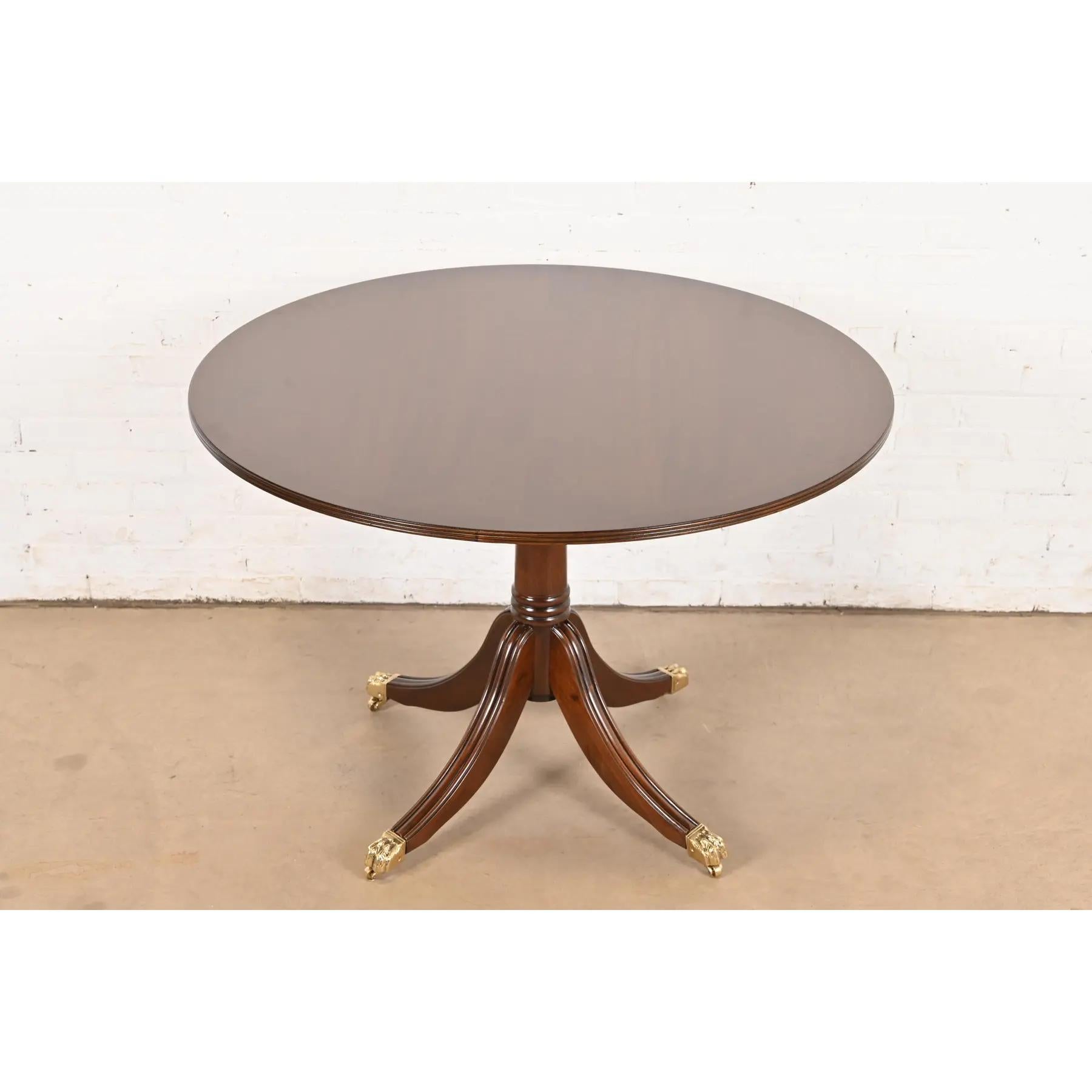 An exceptional Georgian or Regency style pedestal dining table, center table, or breakfast table

In the manner of Baker Furniture

USA, Circa 1980s

Gorgeous banded mahogany, with carved solid mahogany pedestal and brass paw feet on brass